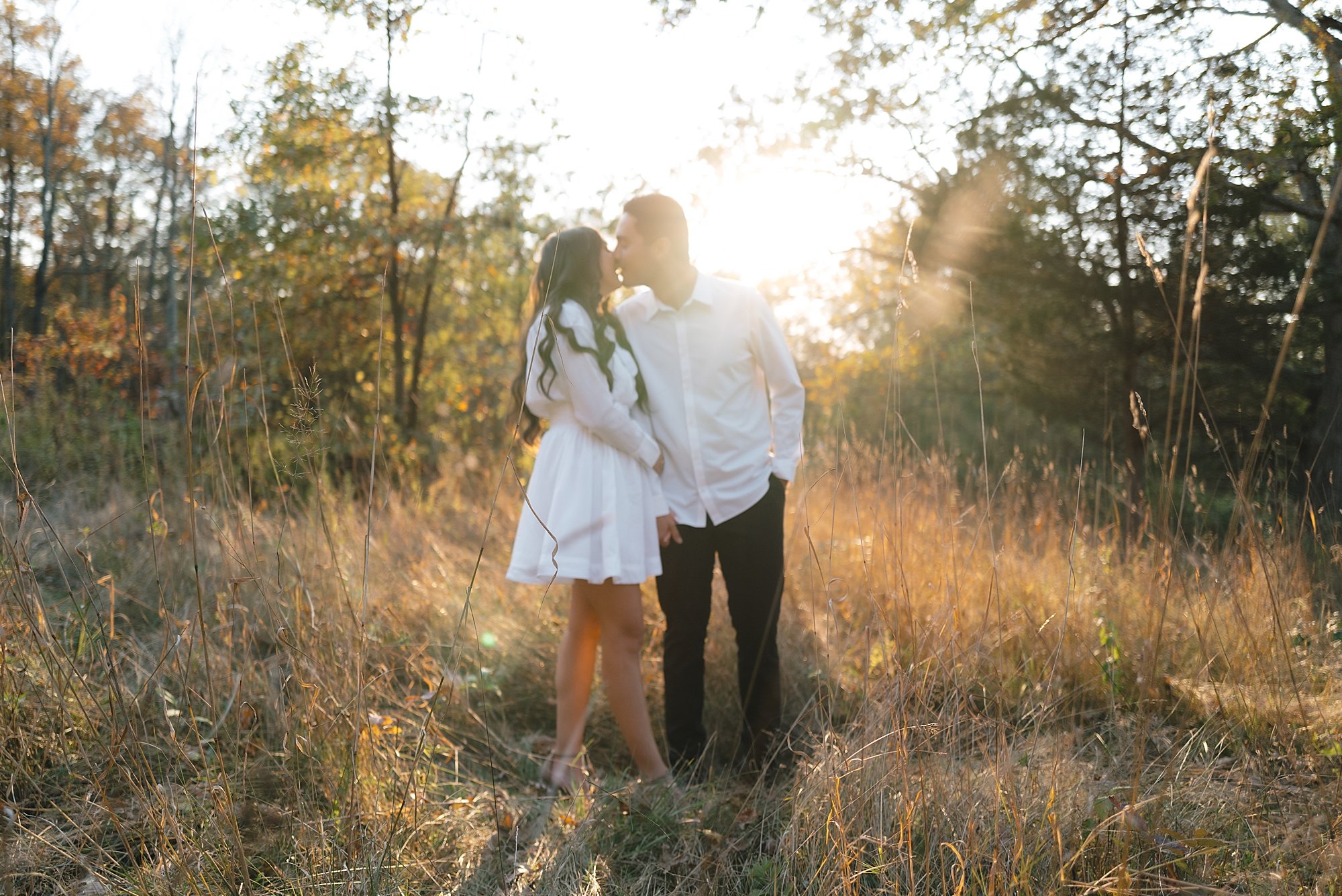 man and woman kiss standing in field at sunset