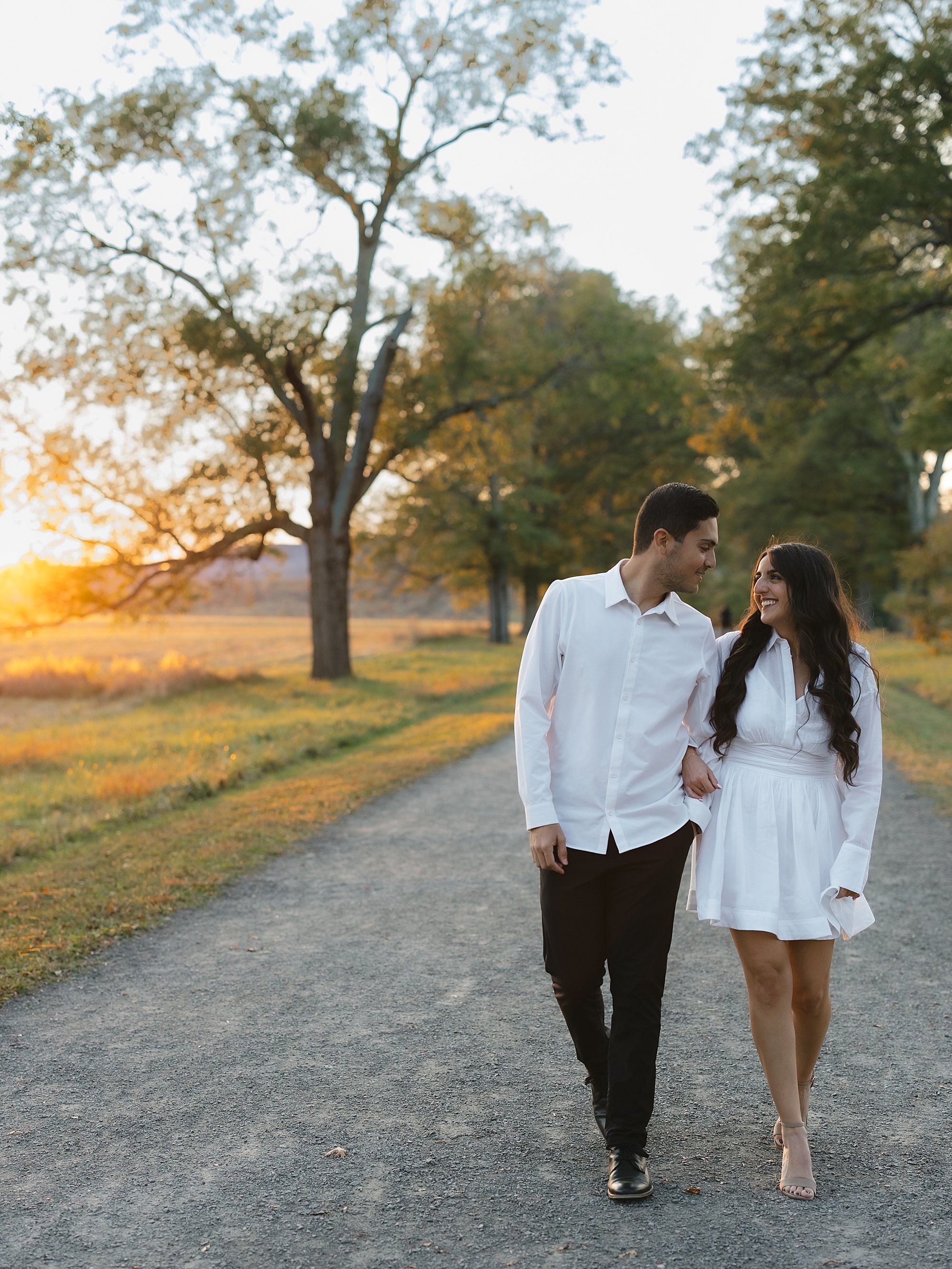couple walks together in white outfits during fall engagement session