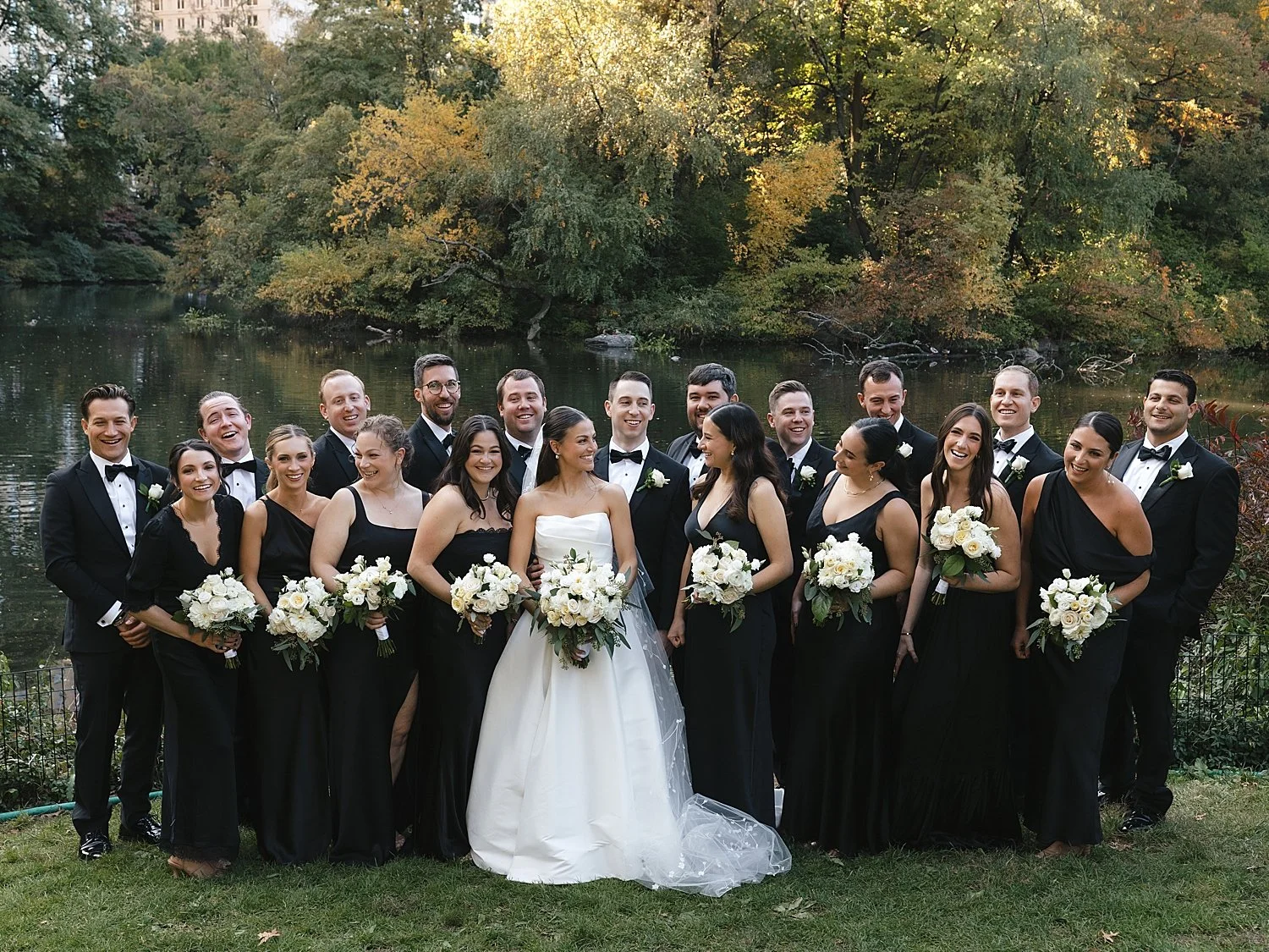 bride and groom stand with wedding party in classic black and white attire in Central Park