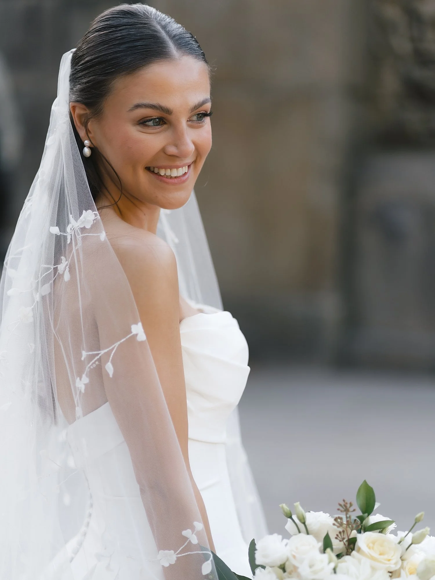 bride smiles in strapless wedding gown holding bouquet of flowers on Bethesda Terrace in Central Park