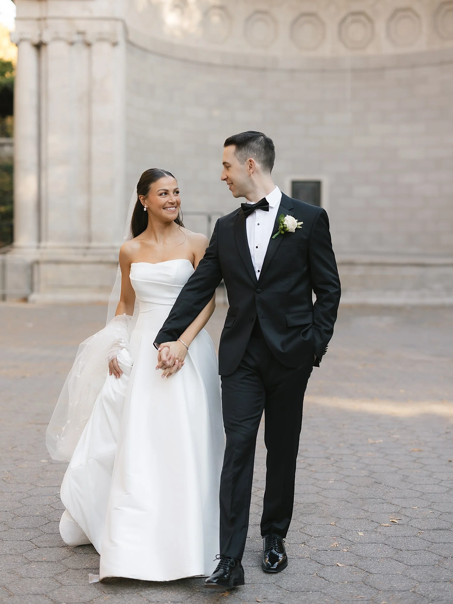 couple holds hands walking through Central Park on their wedding day