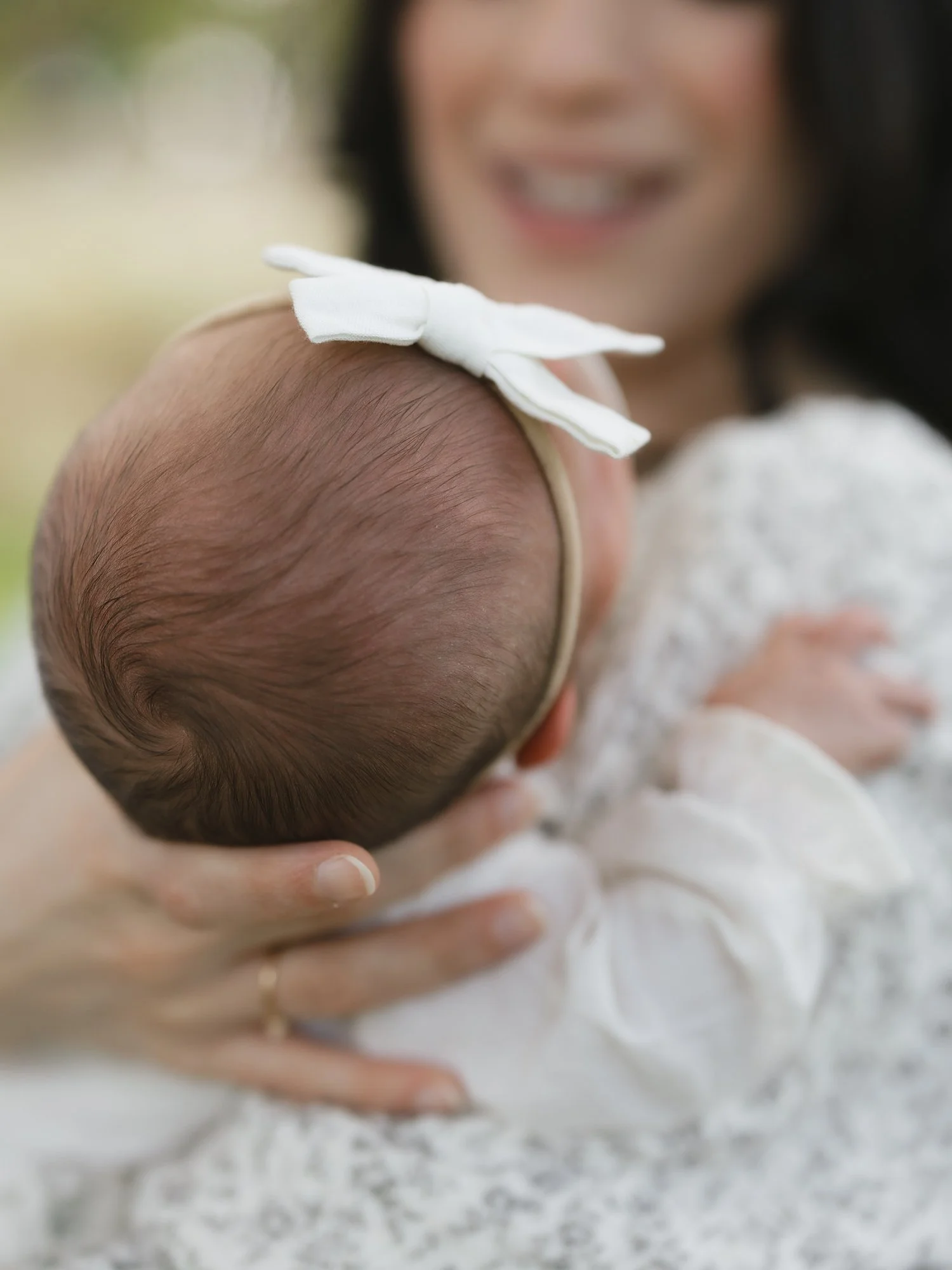 mom holds baby's head with white bow during family portraits at Topsmead State Forest