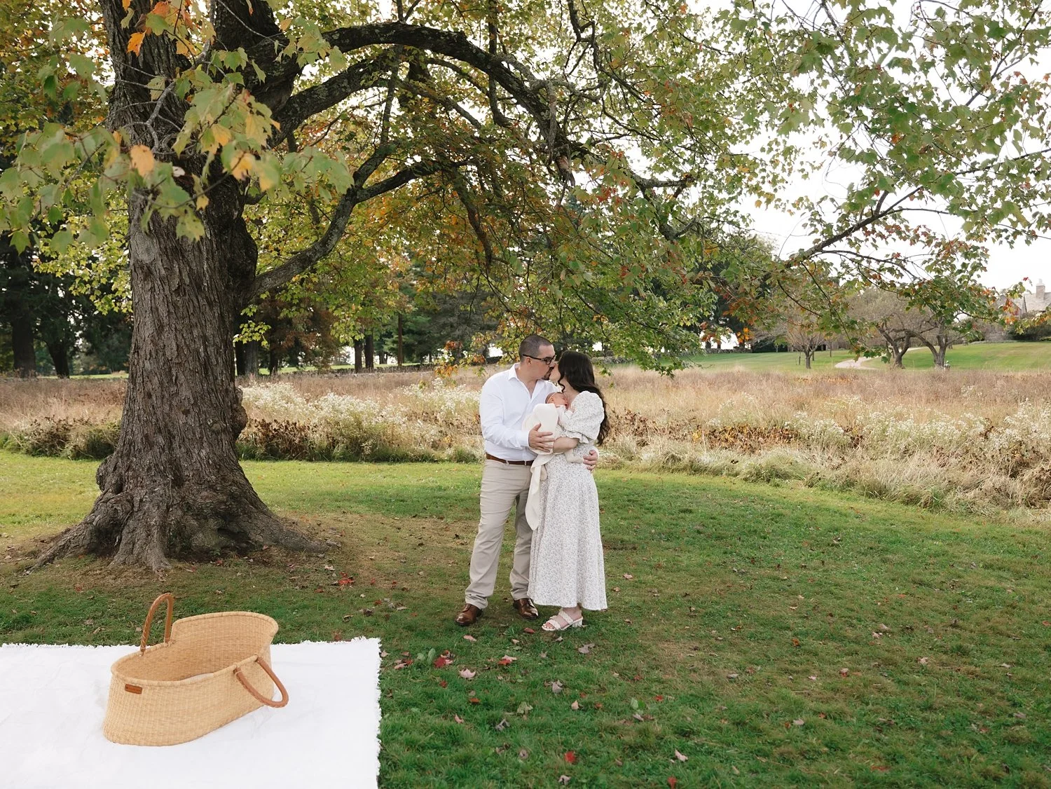 parents snuggle baby under tree near picnic blanket in Topsmead State Forest