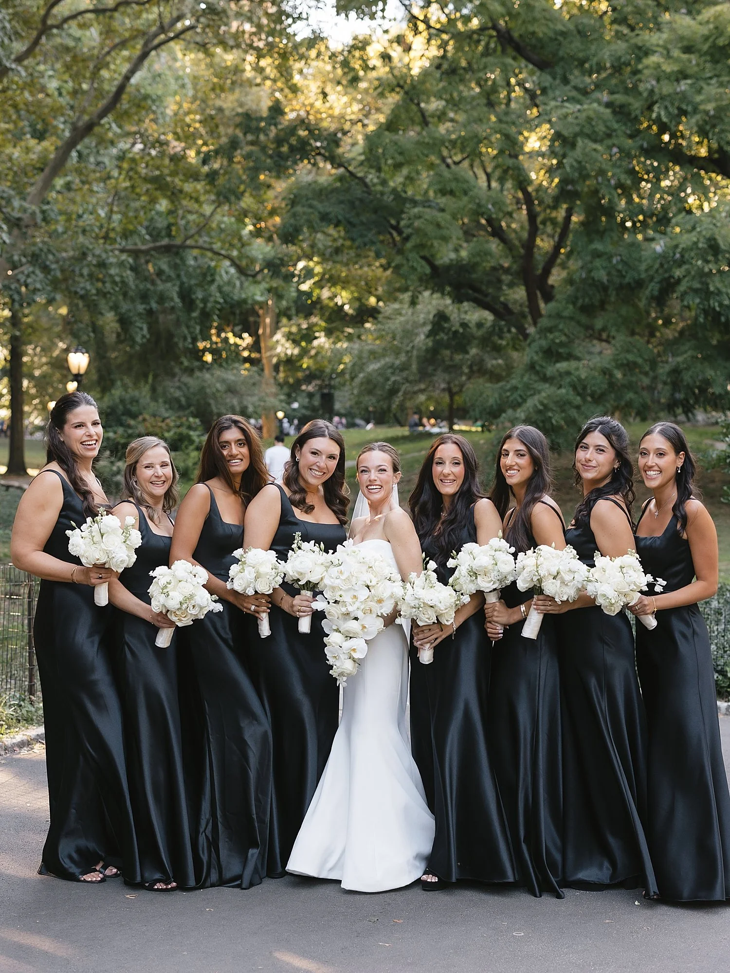 bride poses with bridesmaids in black dresses at Central Park
