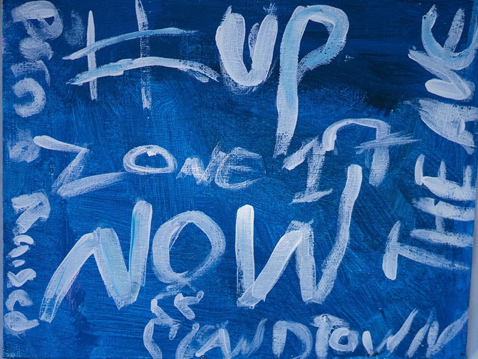 Blue painted canvas with white handwritten words including 'ONE,' 'WILD,' and partially visible other words.