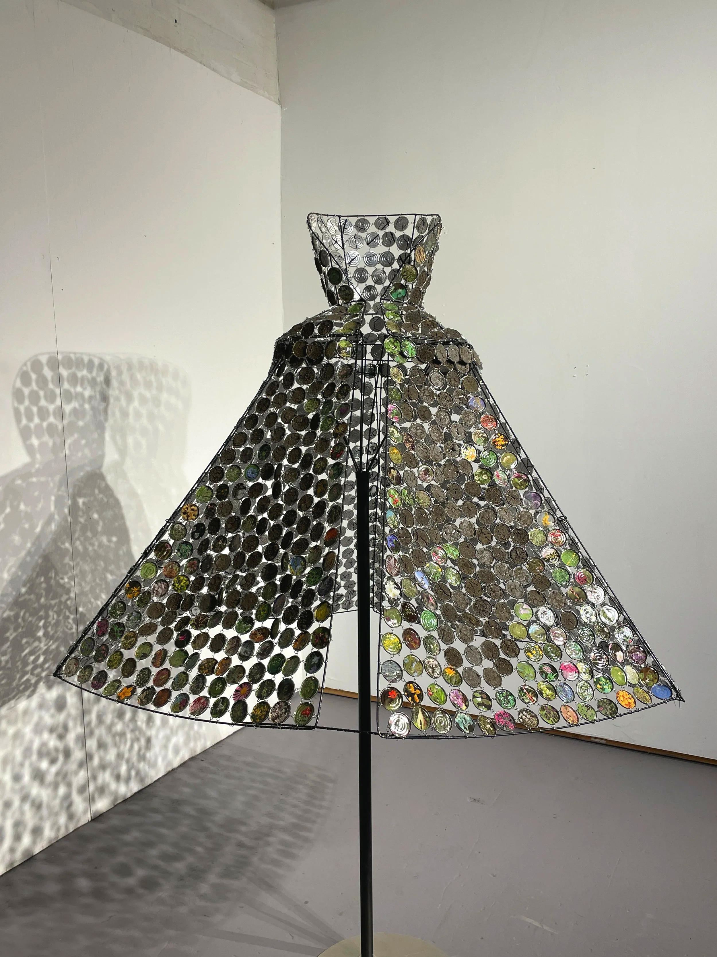 LandsCape
This rigid formal cloak, made up of discarded metal disks linked together, is reminiscent of chain mail. The disks along the bottom edge feature dozens of wildflower photographs, but give way to pans of parched cracked earth at the top edge