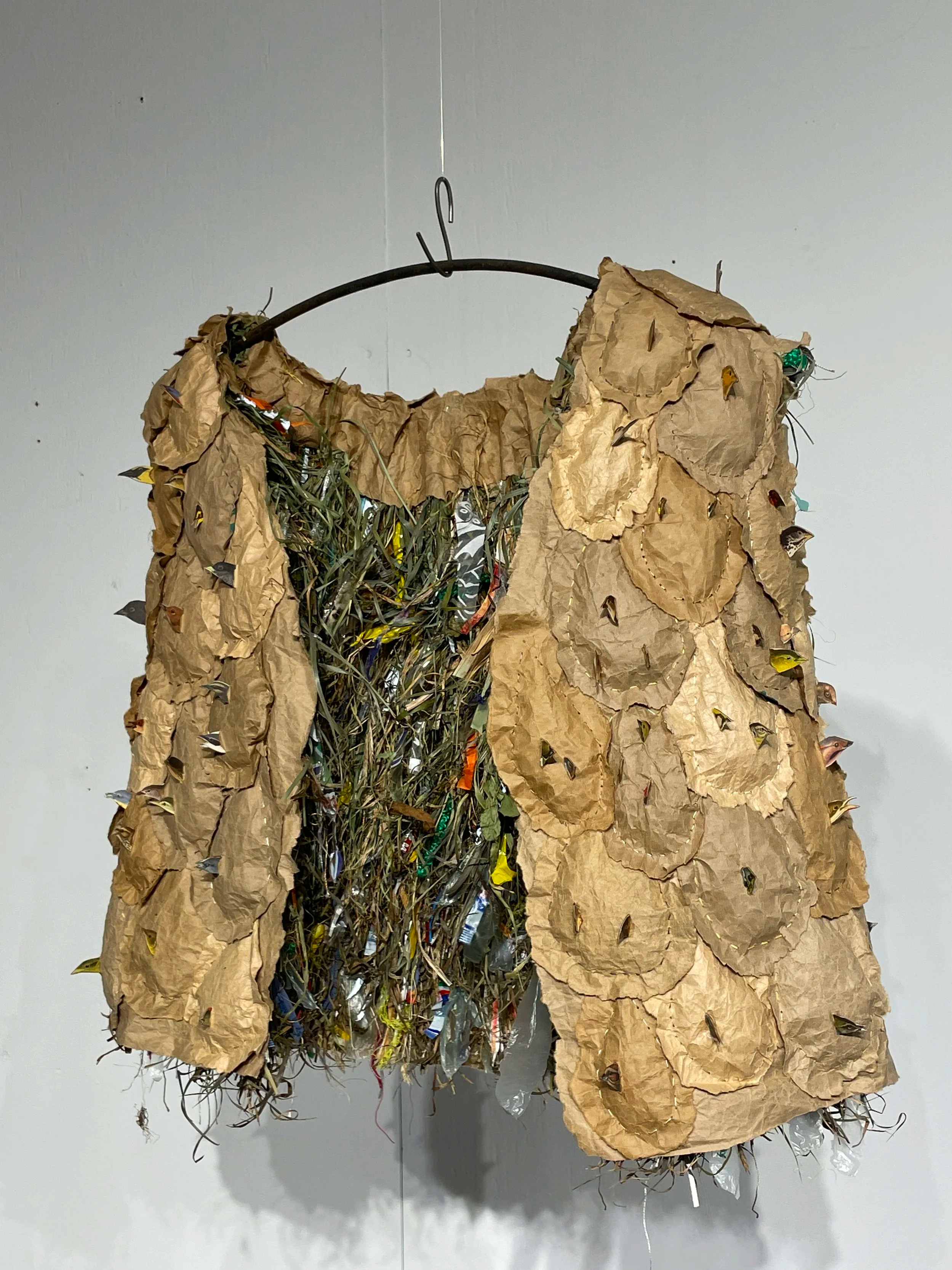 Hunter Gatherer
This flak jacket seems to be a home for birds, made of stuffed paper pouches lined with all the fibers a bird might use to build a nest. Each bird pierces through a pouch, both guarding and hiding; the multitude of beaks create a thor