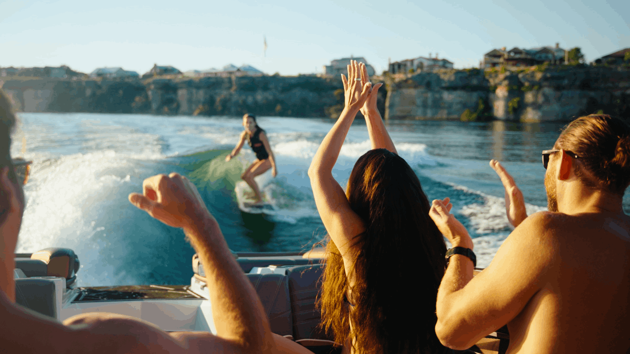 a looping animation of a female is wakesurfing in the background while in the foreground a group of people in the boat are clapping for her