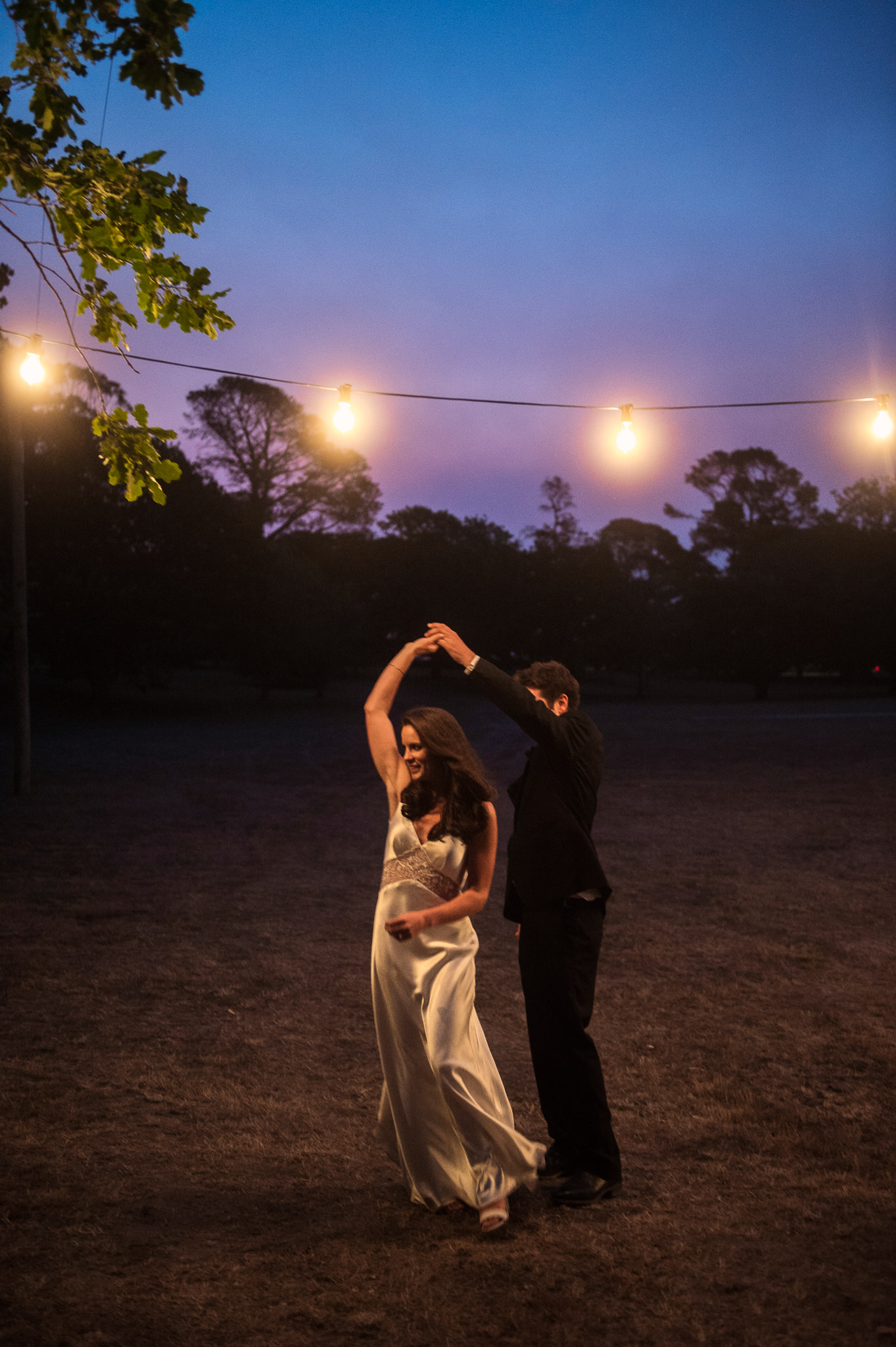  Festoon lighting in the trees surrounding the clear marquee. Bride and groom dancing 