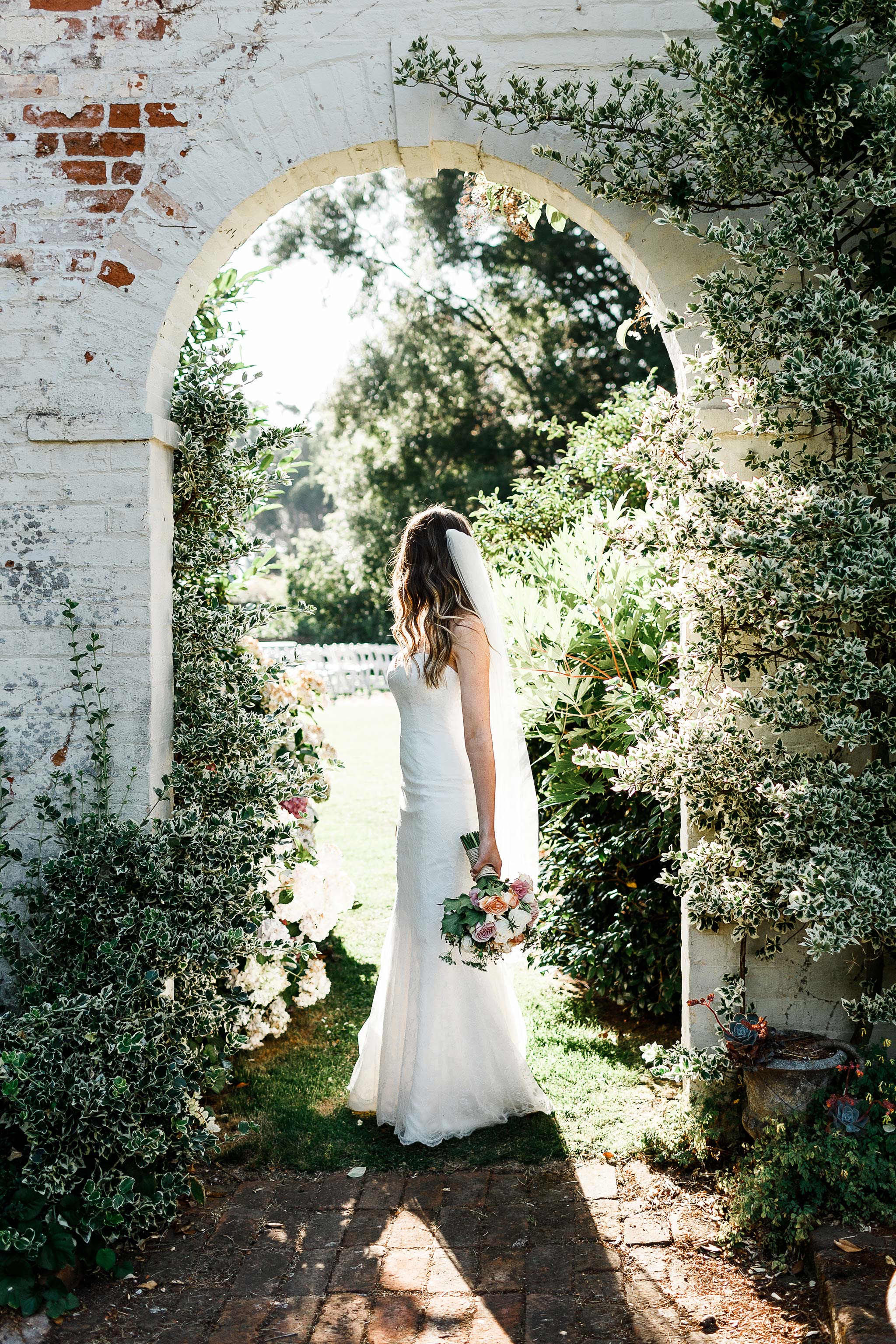  Bride under Brickendon homestead garden arch with bouquet 