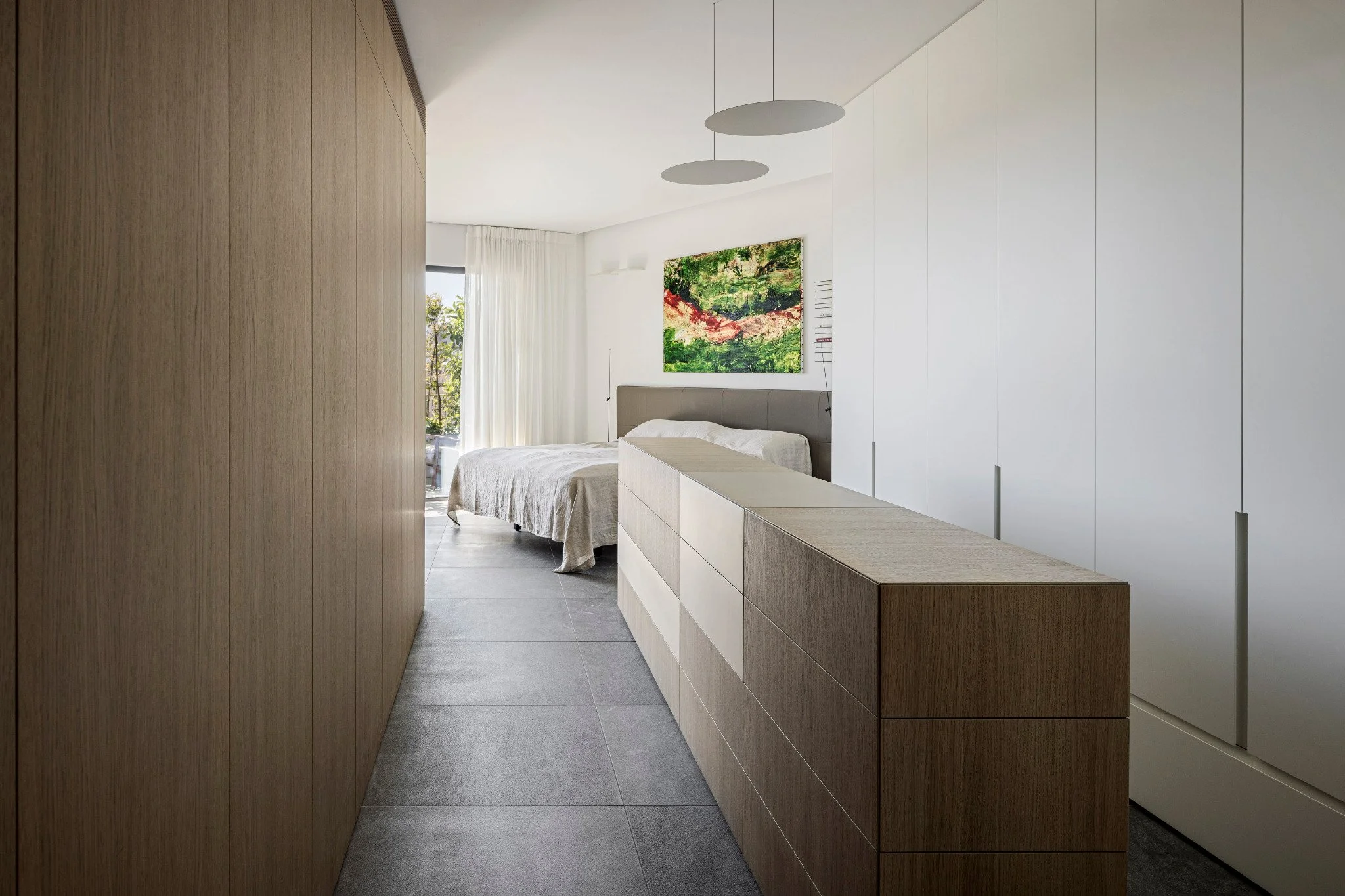 Modern bedroom with a bed, wooden and white cabinets, a painting on the wall, and a window with curtains.