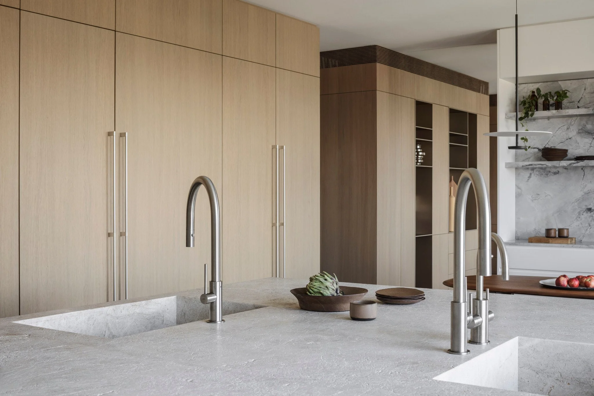 Modern kitchen with light wood cabinets, a marble backsplash, a sink with a stainless steel faucet, and a gray stone countertop.