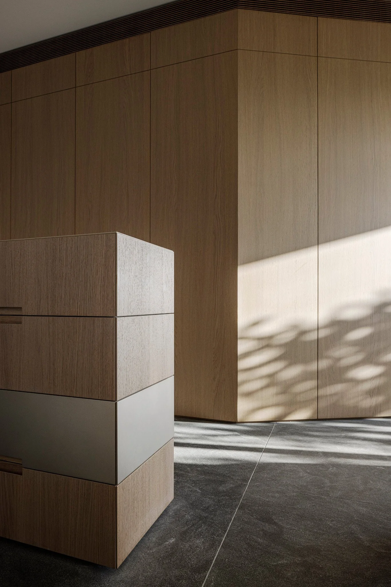 Modern wooden-paneled walls and a cabinet in a well-lit interior space with shadows cast on the floor.
