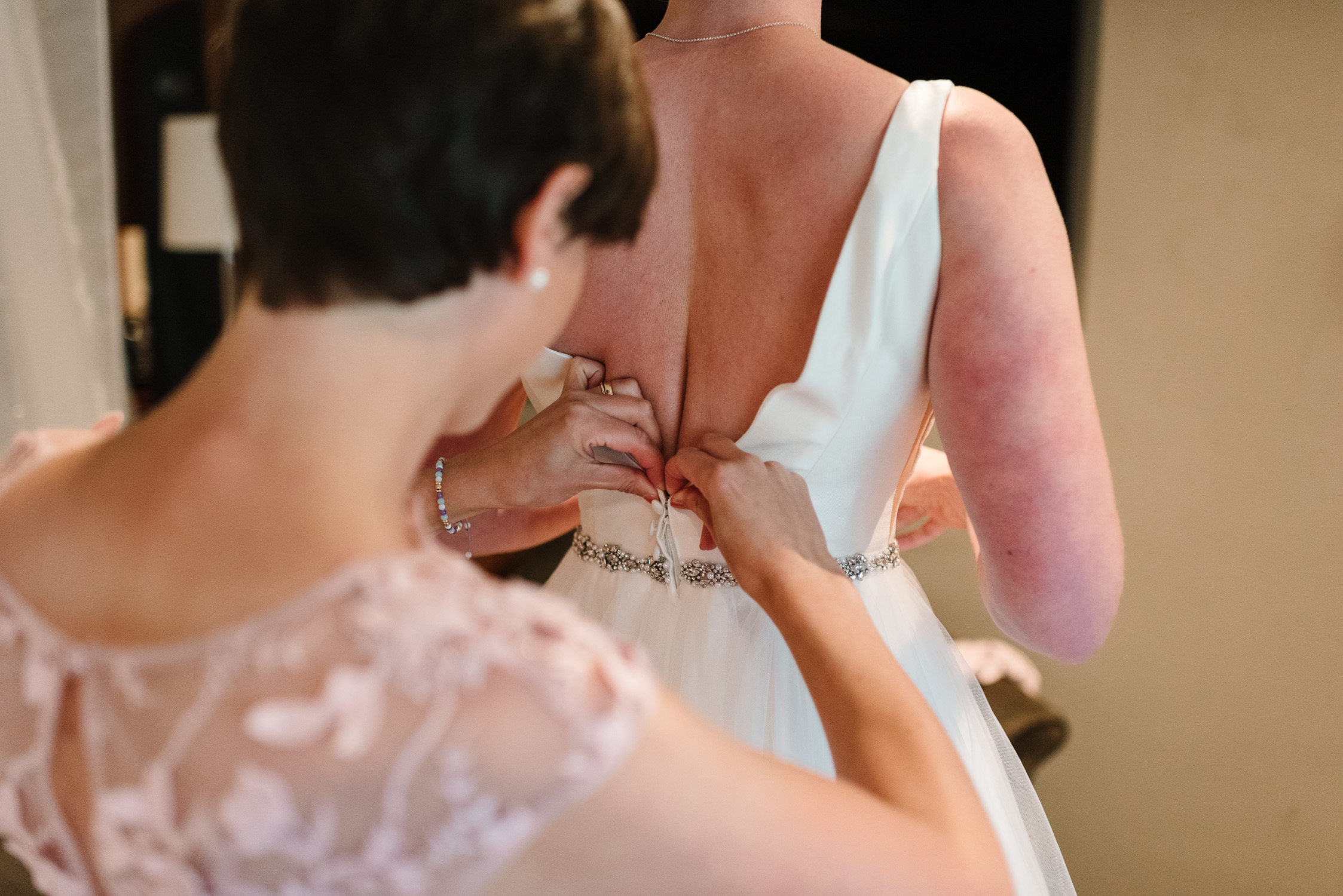 bridesmaid zipping up bride's dress in hotel room