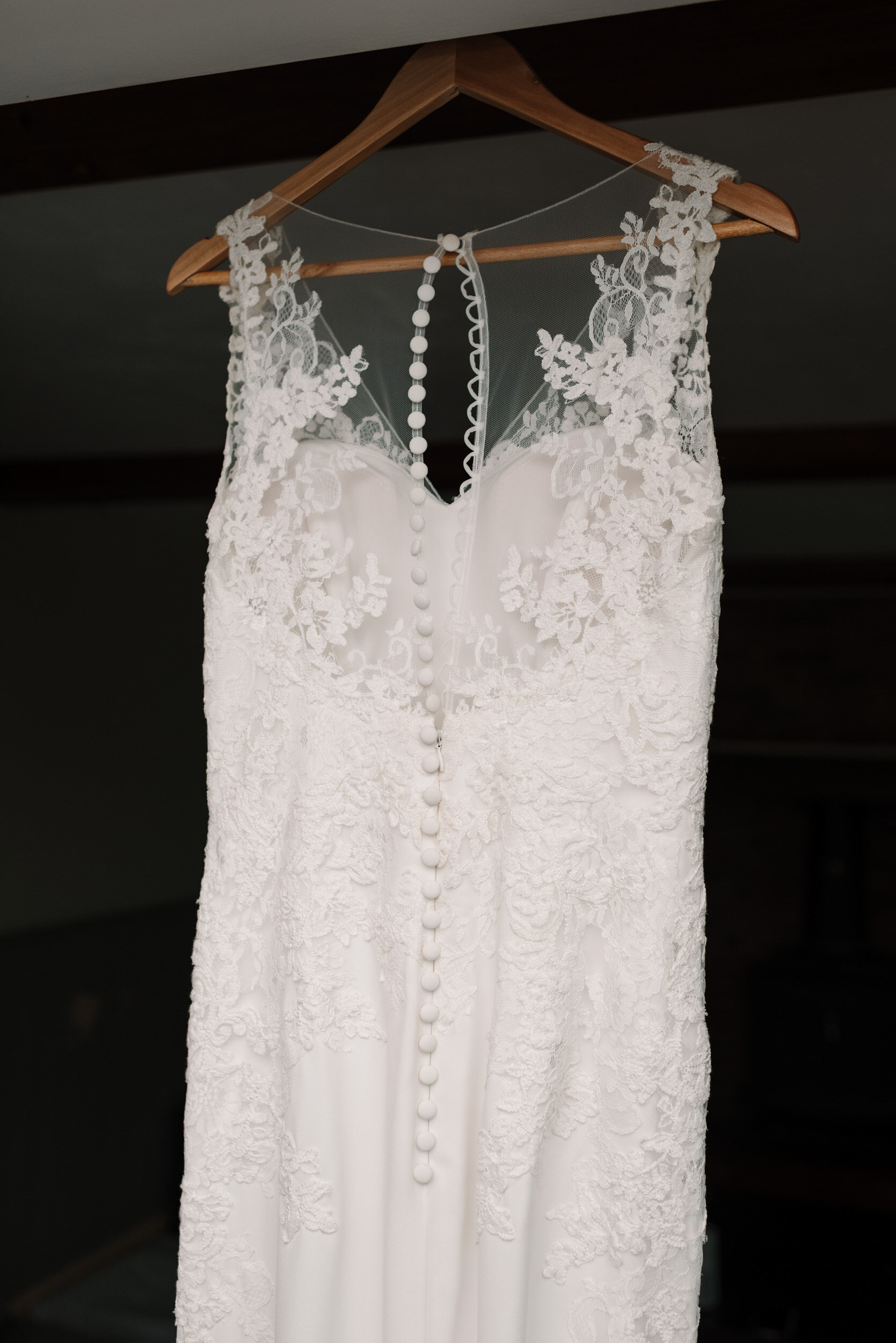 Bride's white dress with lace and small buttons, hanging from doorframe