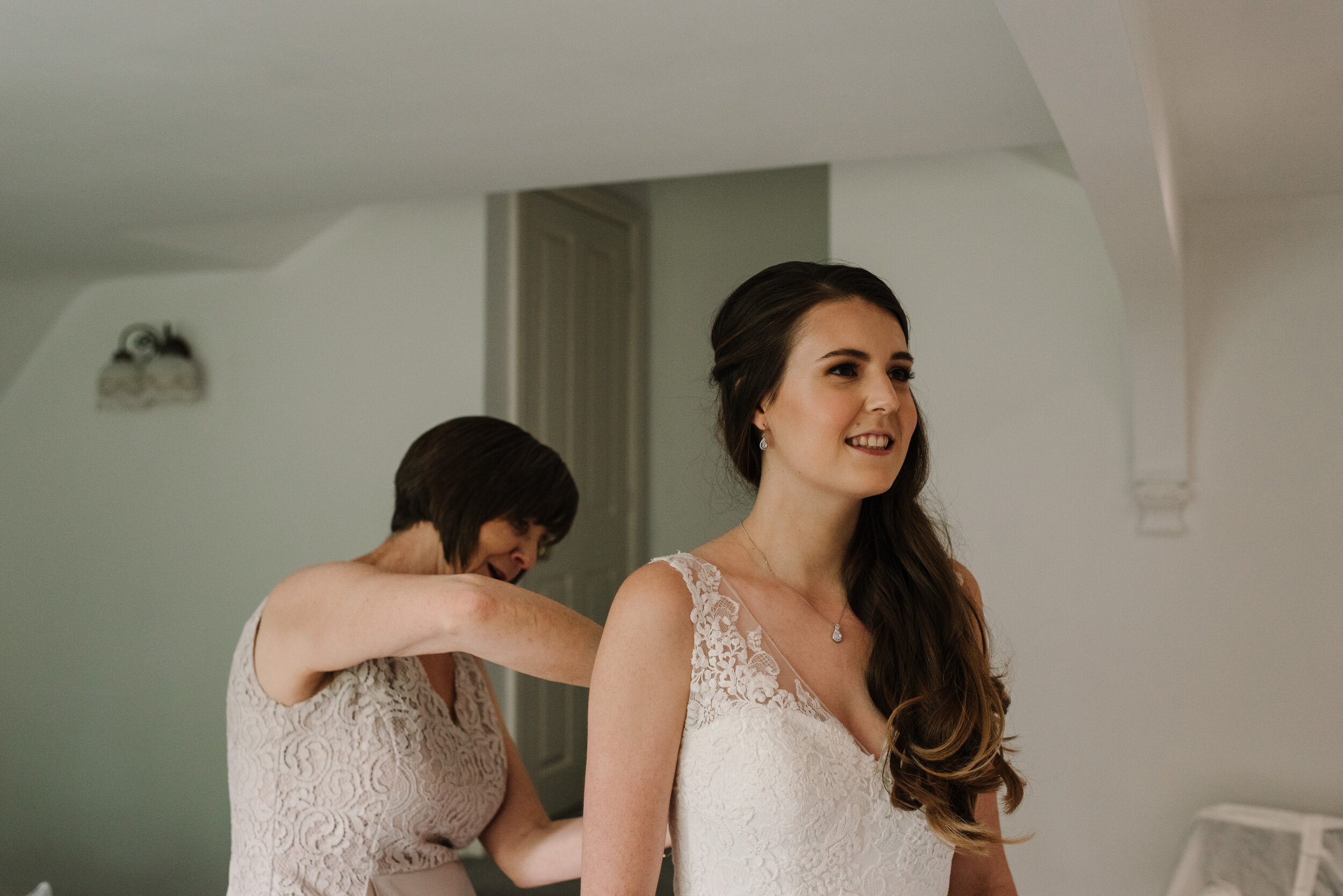 Mother buttoning up her daughter's bridal dress