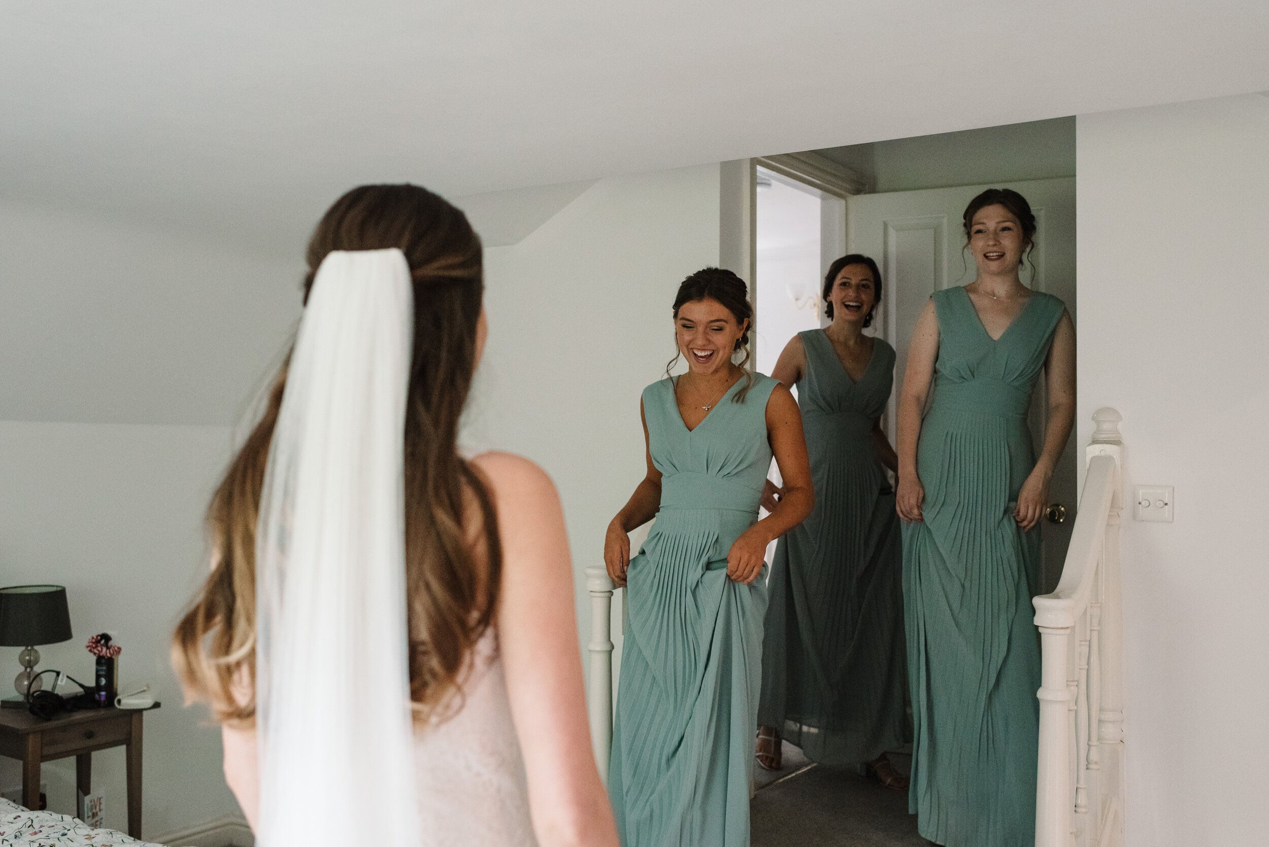 Three bridesmaids seeing their friend in her bridal outfit and smiling