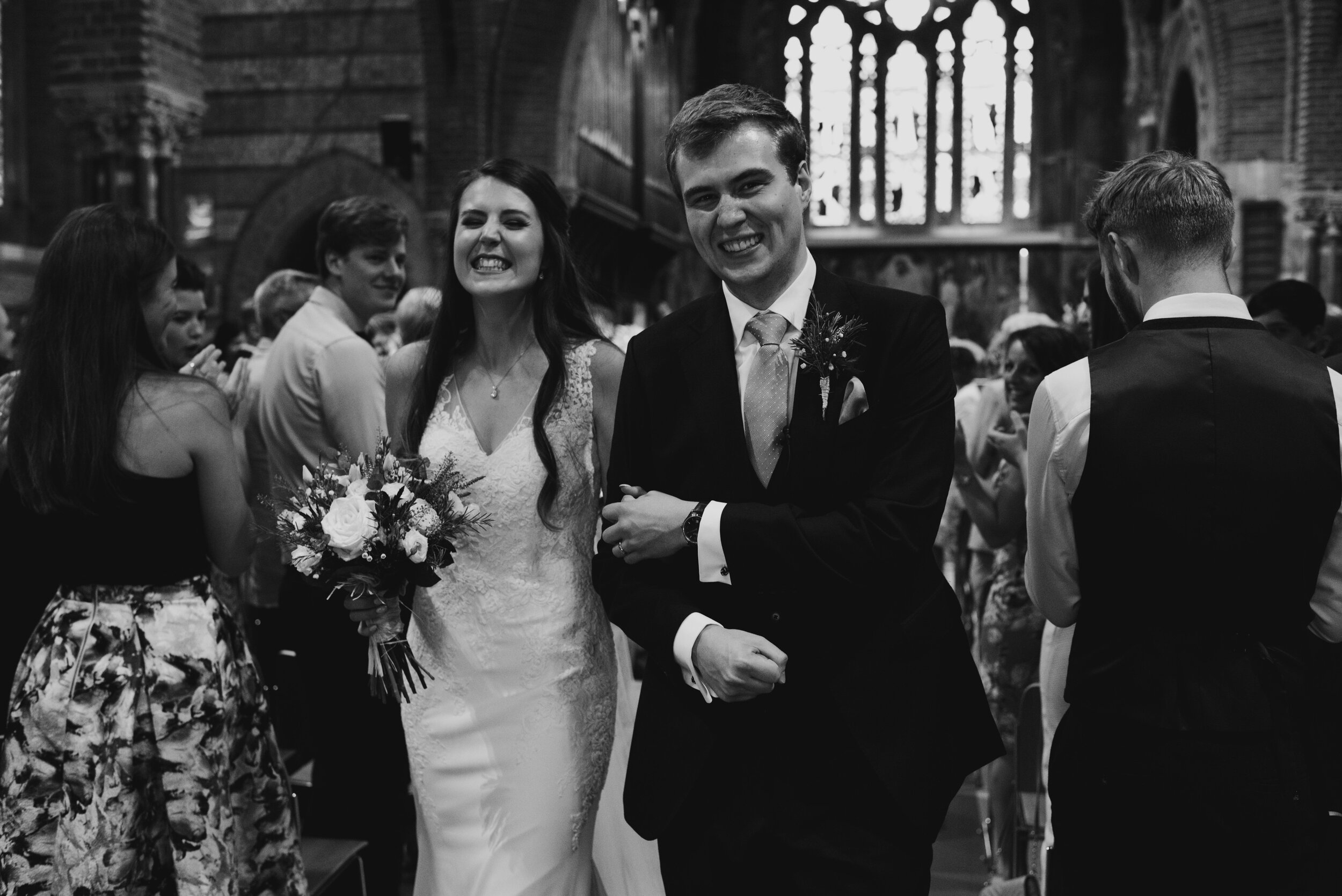 Black and white photo of bride and groom walking down church aisle