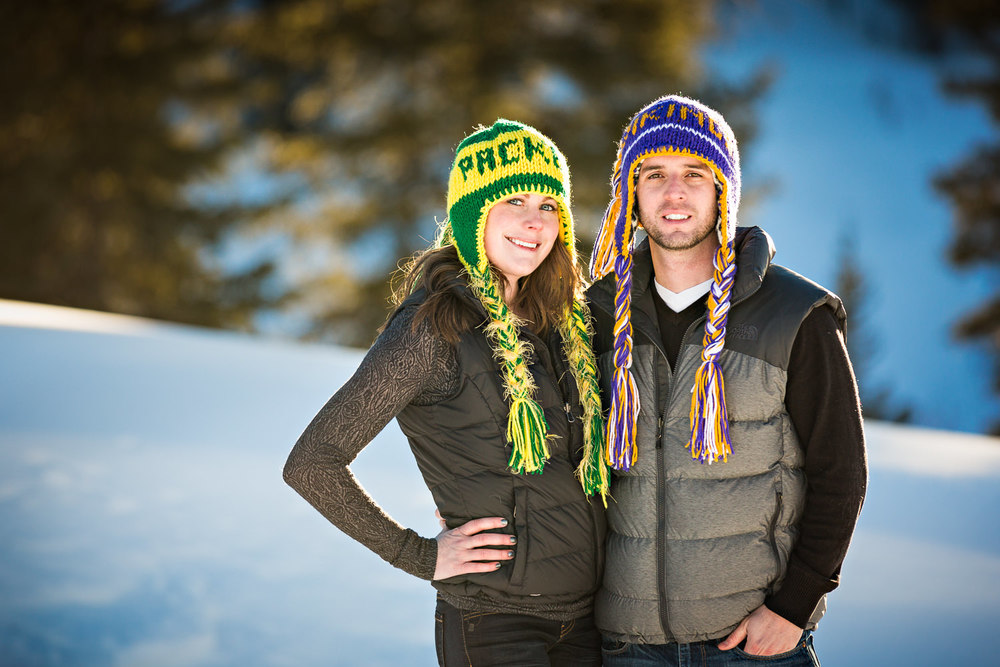big-sky-montana-winter-engagement-session-couple-smiling-with-football-hats.jpg