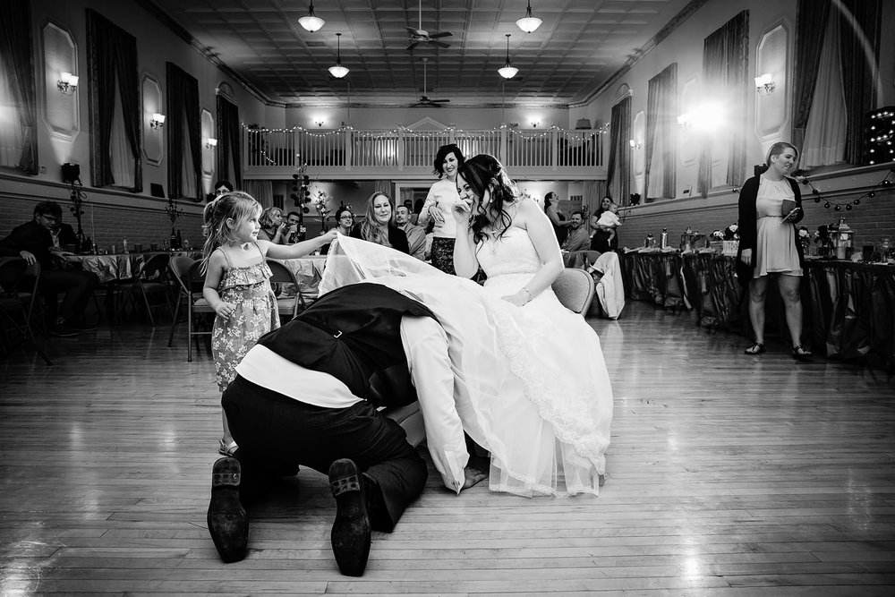 heritage-hall-missoula-montana-bride-laughs-while-flowergirl-helps-remove-garter.jpg