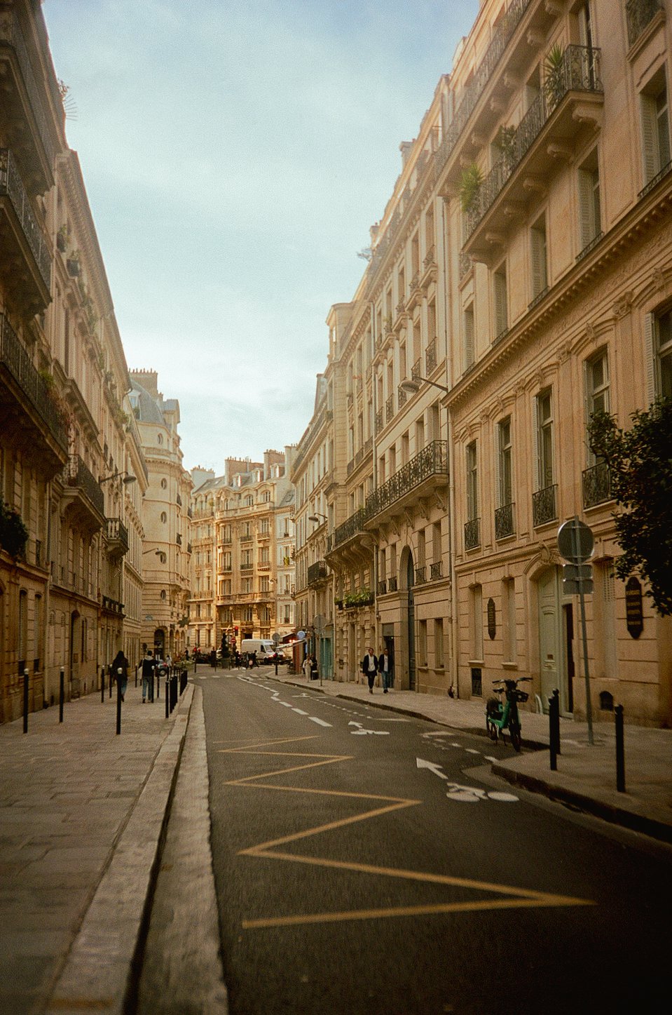 Parisian city street with classic architecture, pedestrians, and parked bicycles.