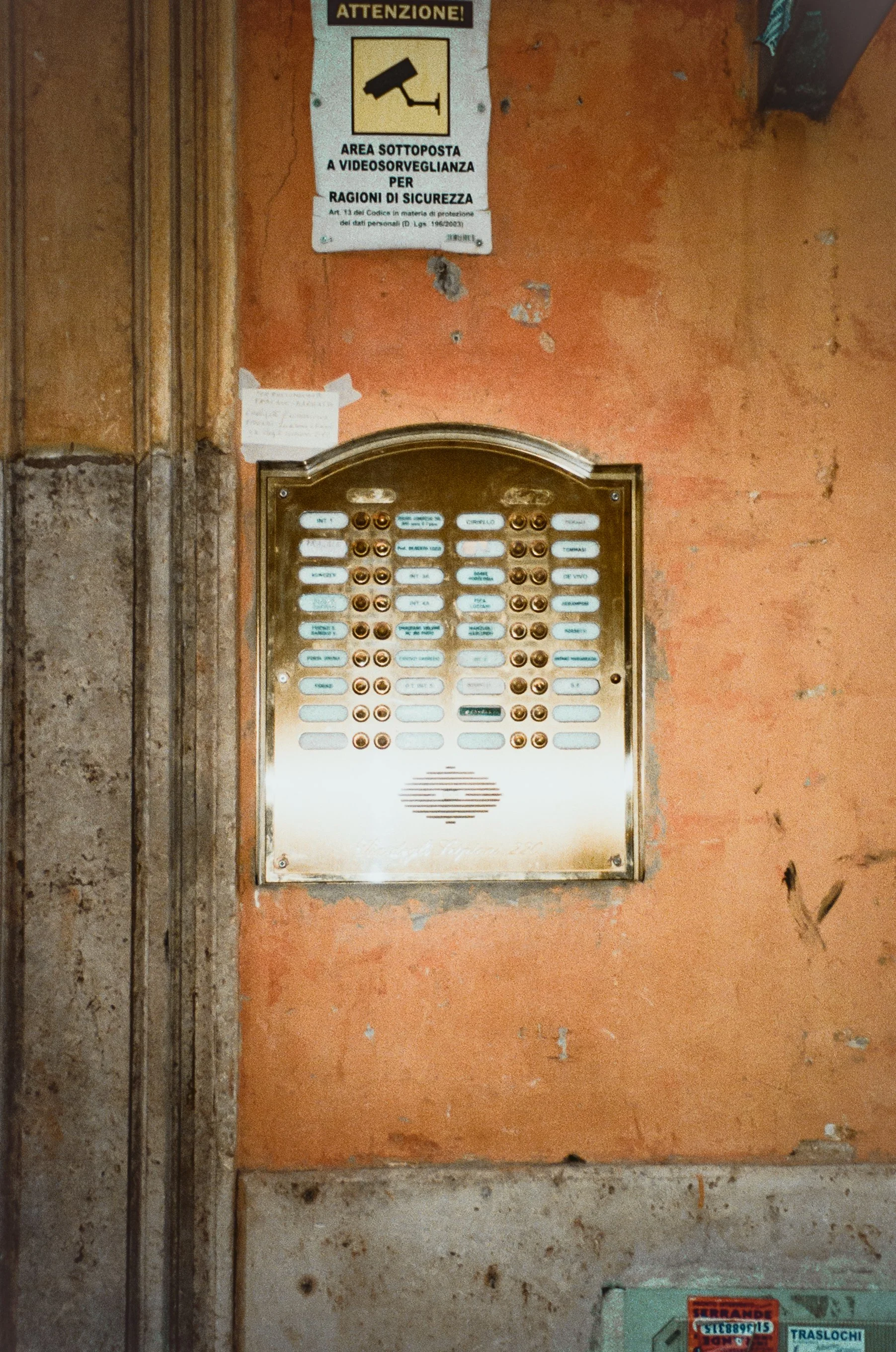 An intercom panel mounted on an orange wall with a surveillance warning sign above it.