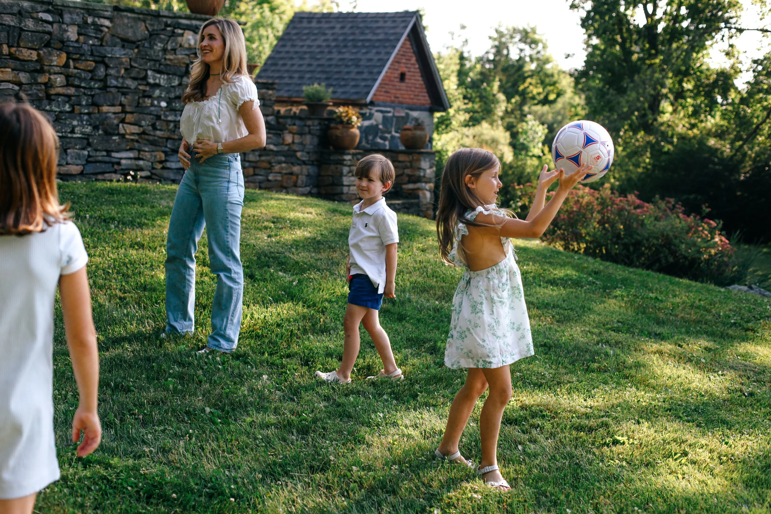 A woman and three children playing football in a backyard garden