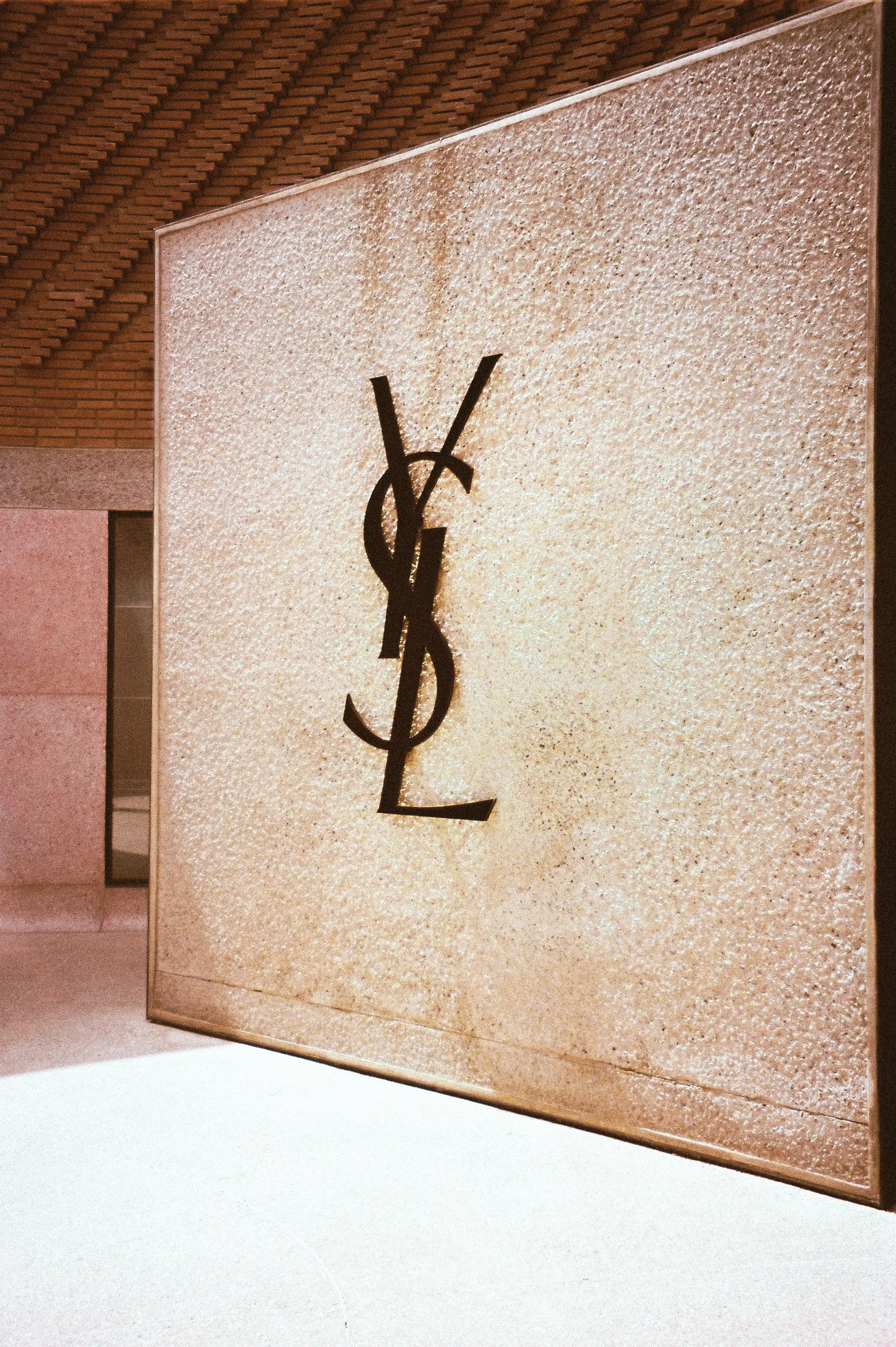 A large wall display with the Yves Saint Laurent logo, featuring black YSL letters on a textured beige background.