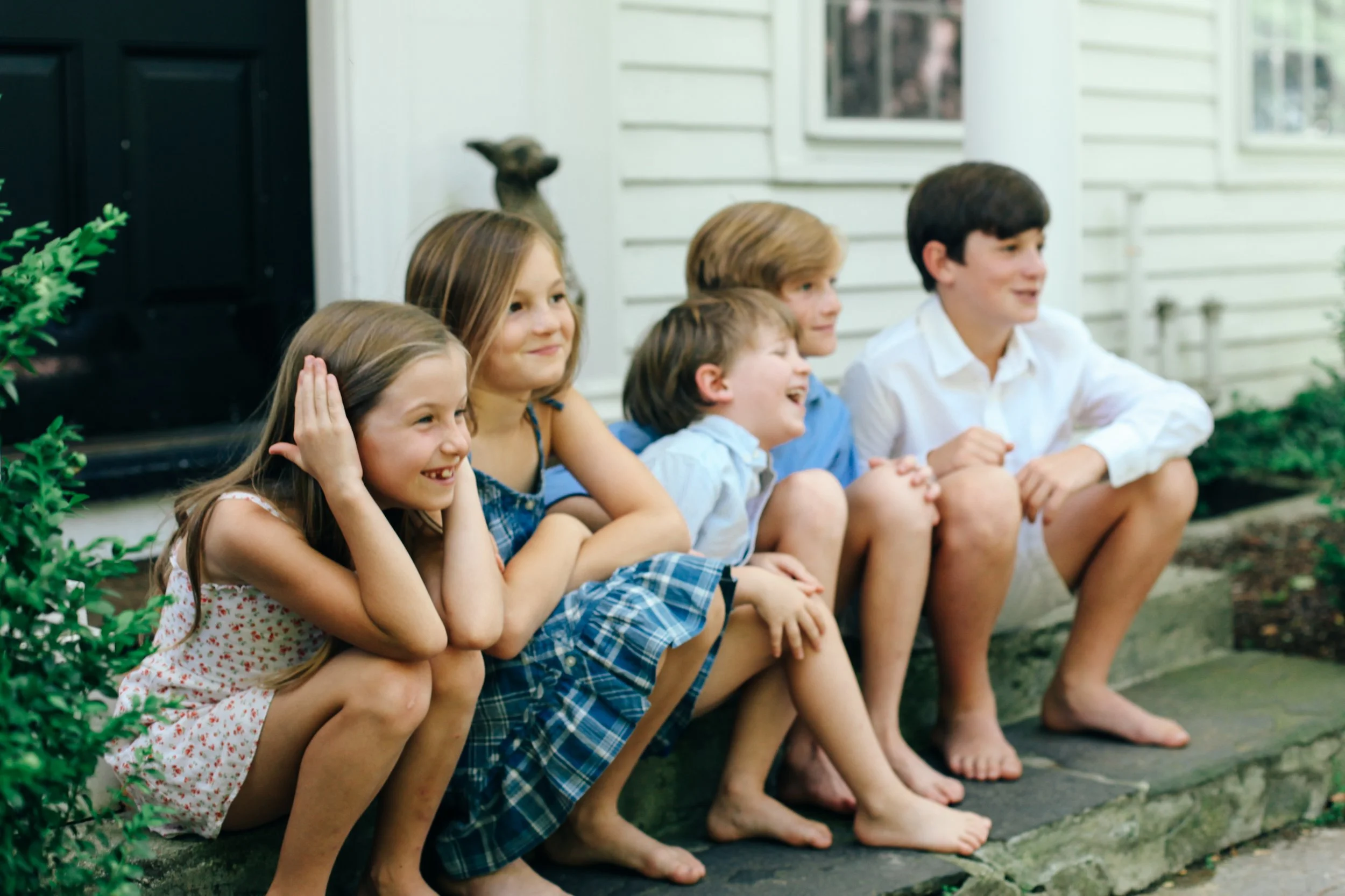A group of children sitting on the porch steps of a house, smiling and laughing.