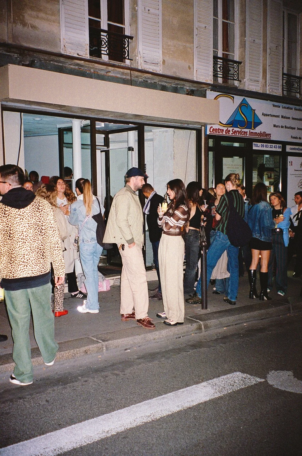 Group of people standing outside a building on a city street at night, some using their phones.