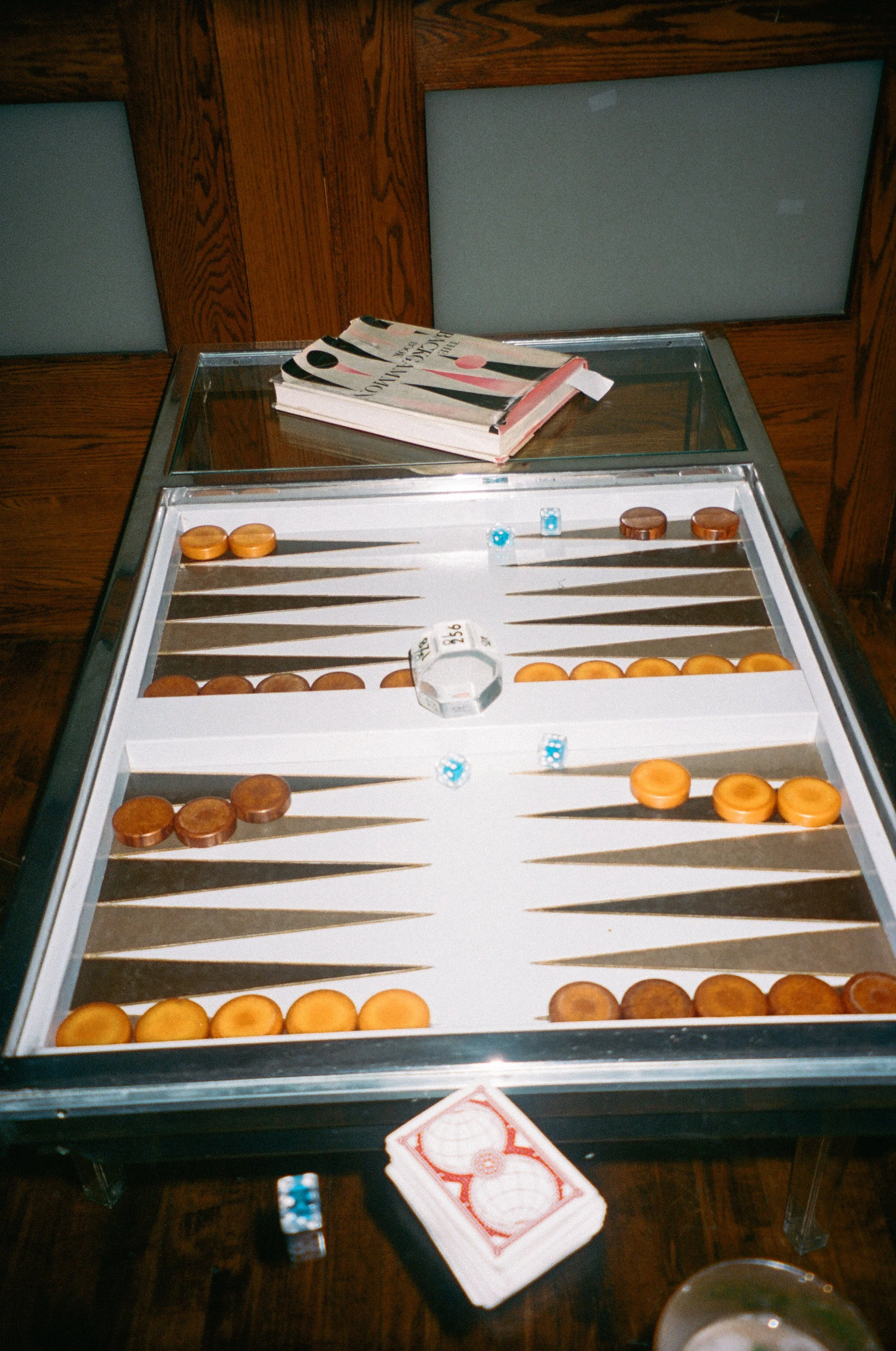 A backgammon game setup on a table with dice and a stack of playing cards nearby.