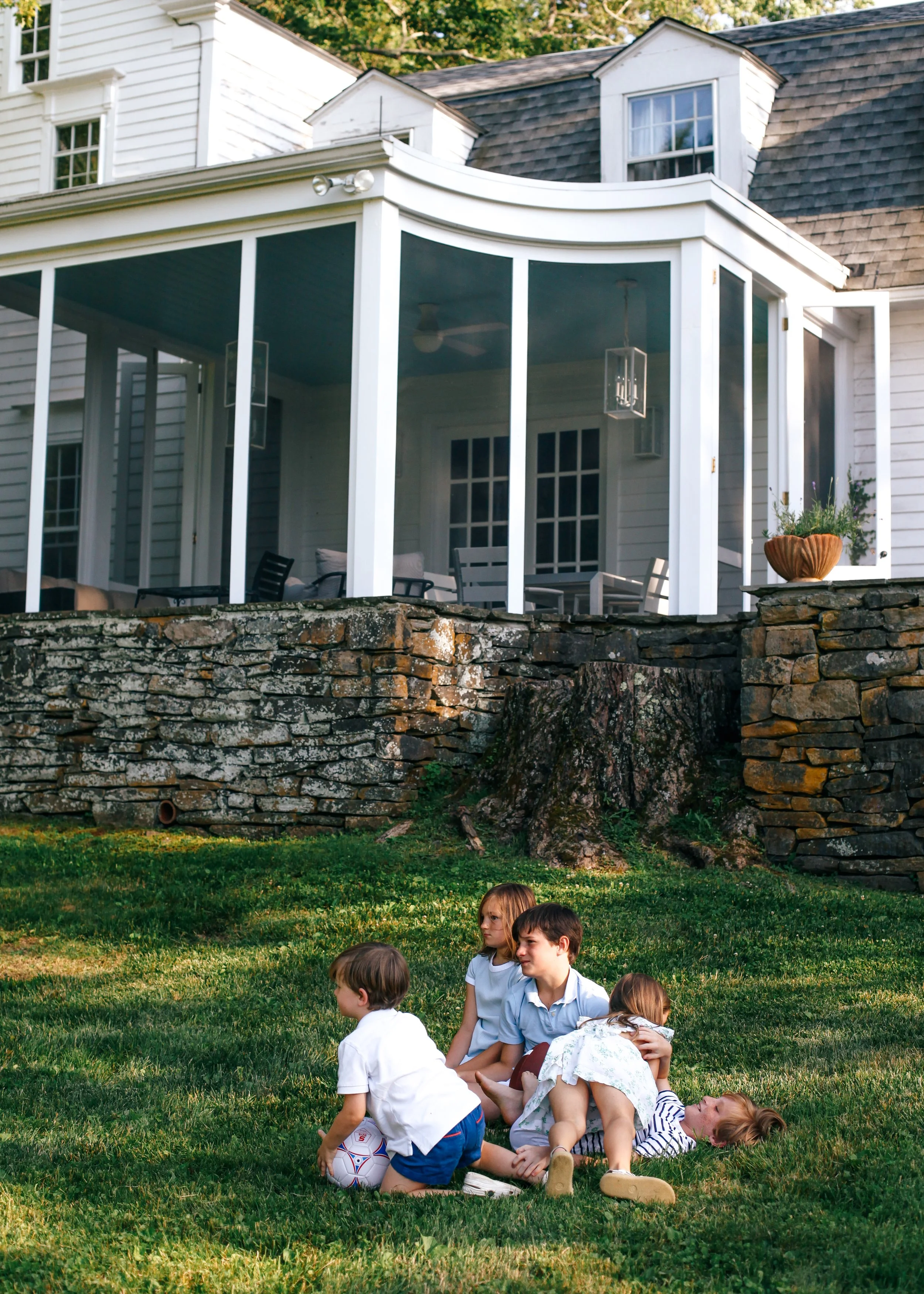 Group of children playing on grass in front of a house with a sunroom in the backyard.