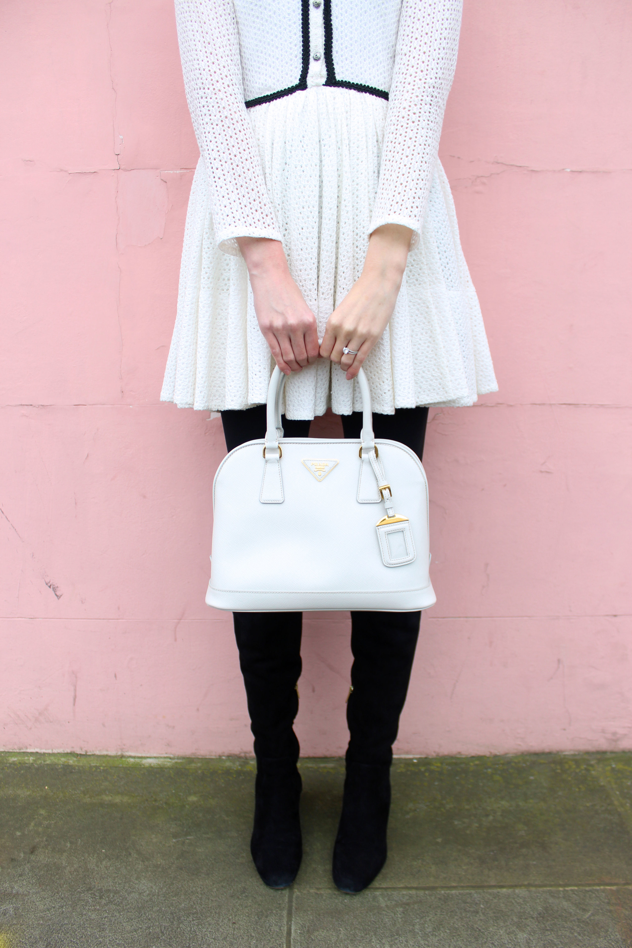 Prada bag, suede over the knee boots, and a white lace dress, all in front of a pink wall in Notting Hill.