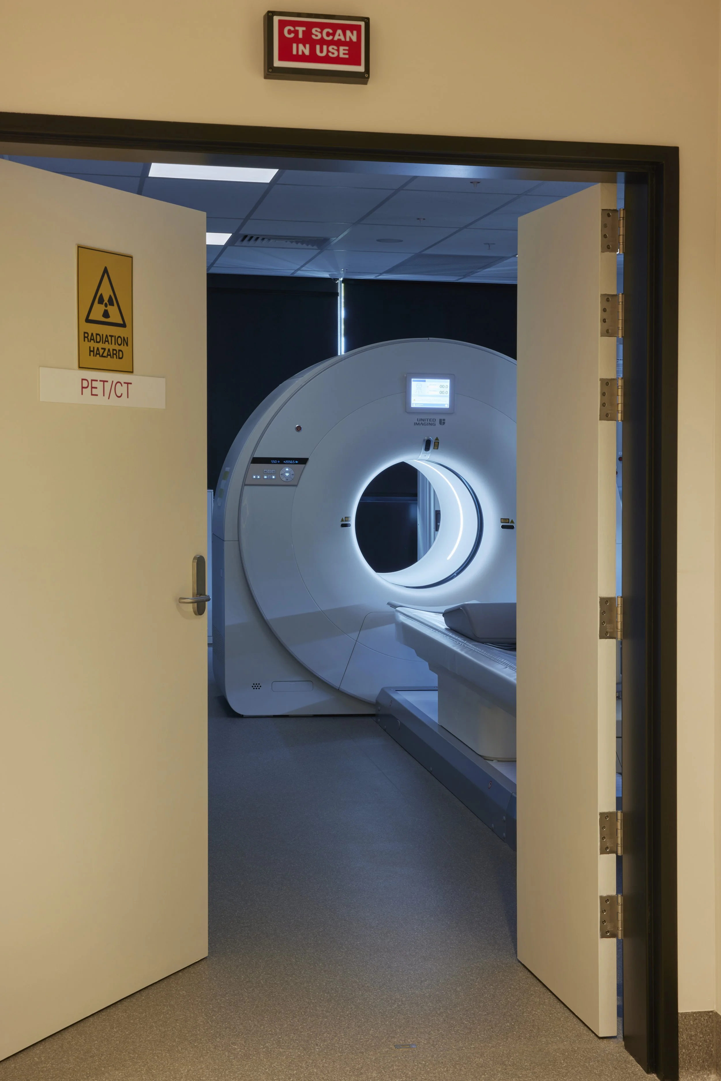 Hospital room with an open door revealing an MRI machine, a radiation hazard sign, and a CT scan sign above the door.