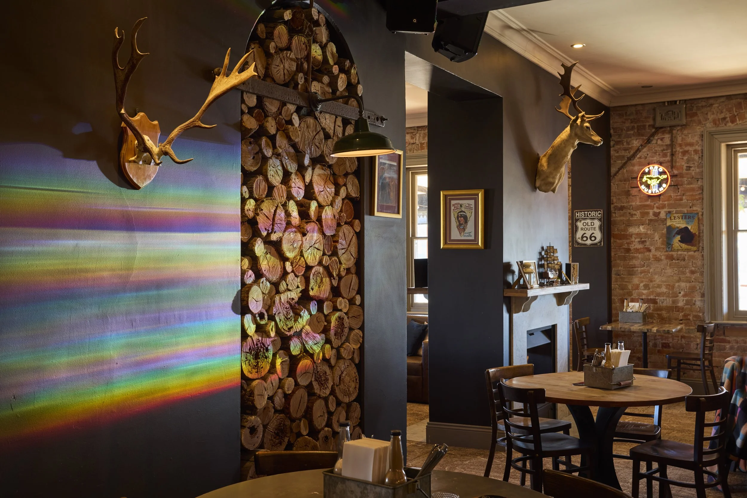 Interior of a rustic restaurant with wooden log decor, mounted animal antlers, a brick wall, and vintage signs.
