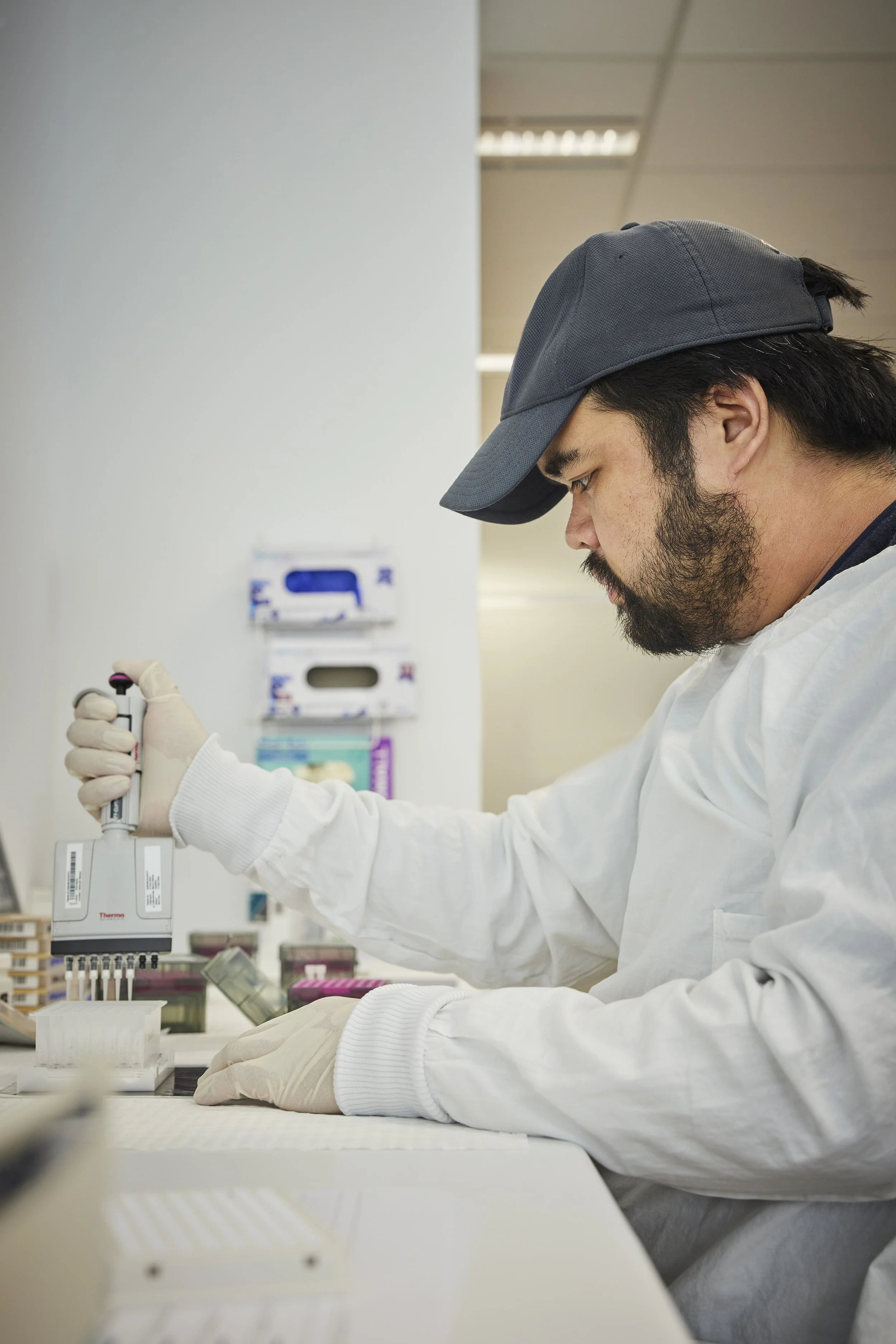 A scientist in a white lab coat and gloves using a pipette in a laboratory with testing supplies.