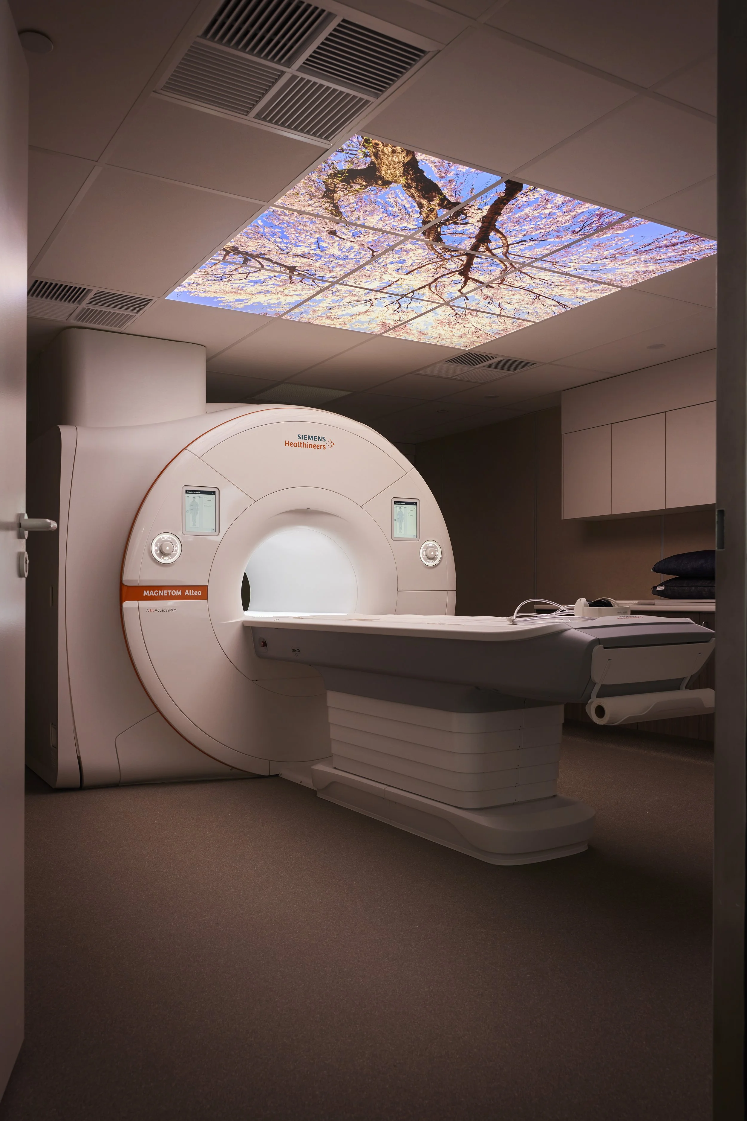 A Siemens Healthineers MRI machine in a hospital room with a ceiling photo of cherry blossoms and a blue sky.