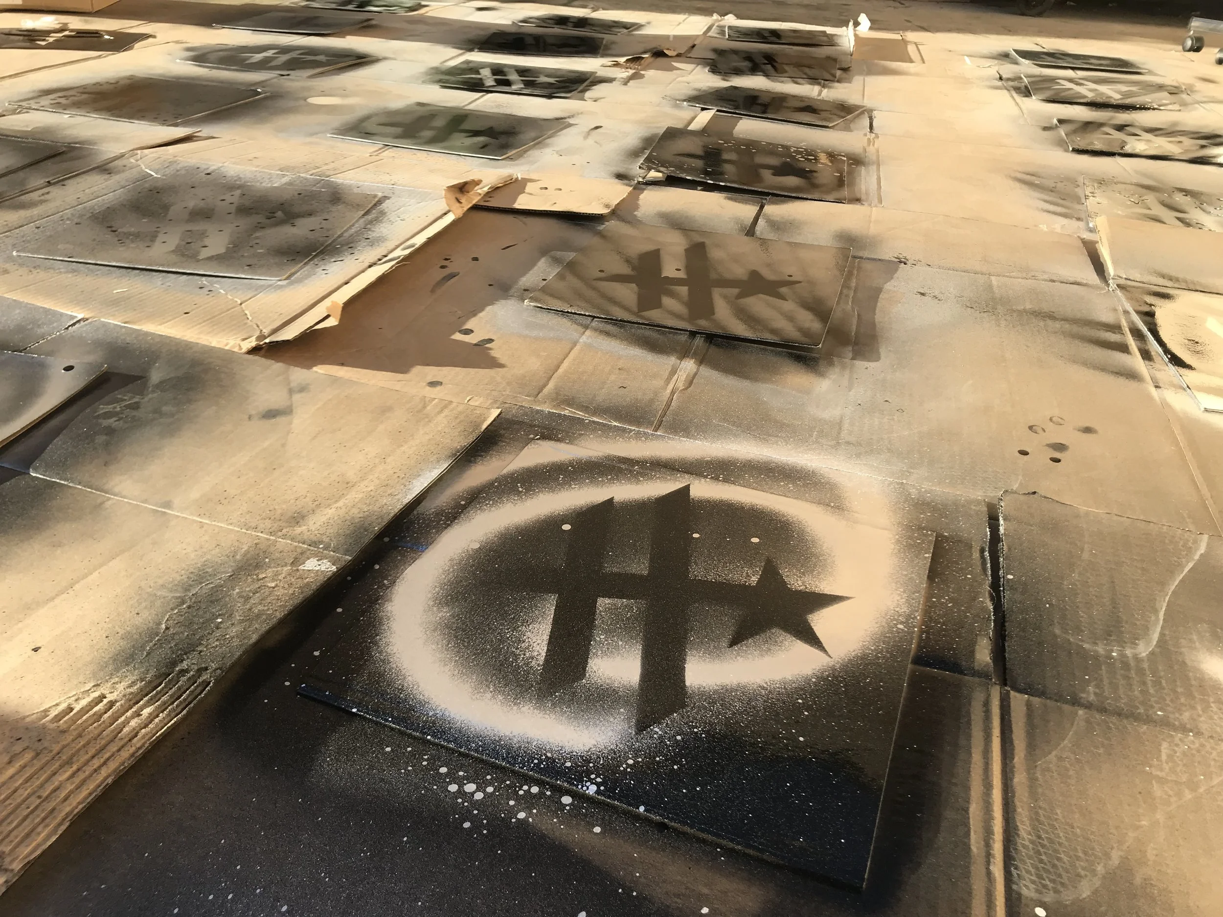 Spray-painted stencil art on cardboard and wood surfaces with a black background, featuring a circle and an 'H' and a star.