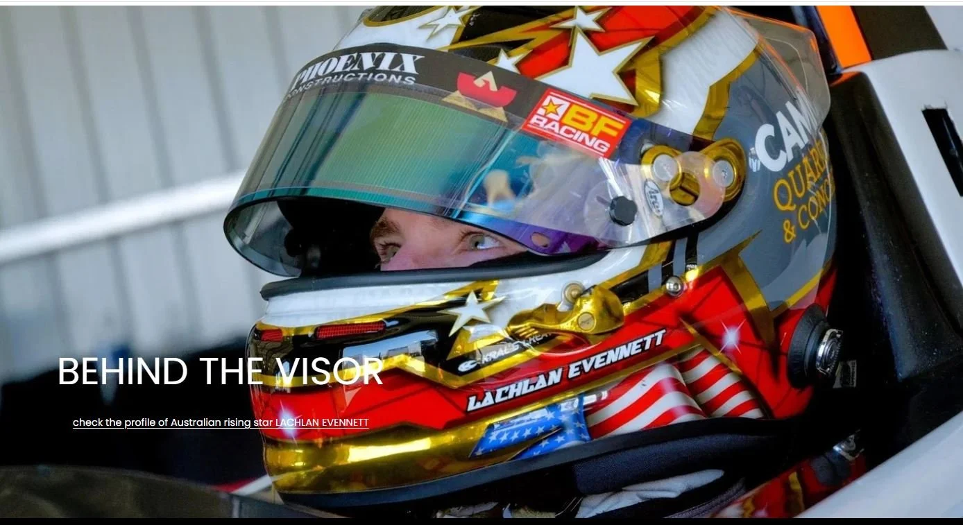 Close-up of a race car driver wearing a helmet with star and American flag designs, sitting in a racing car.