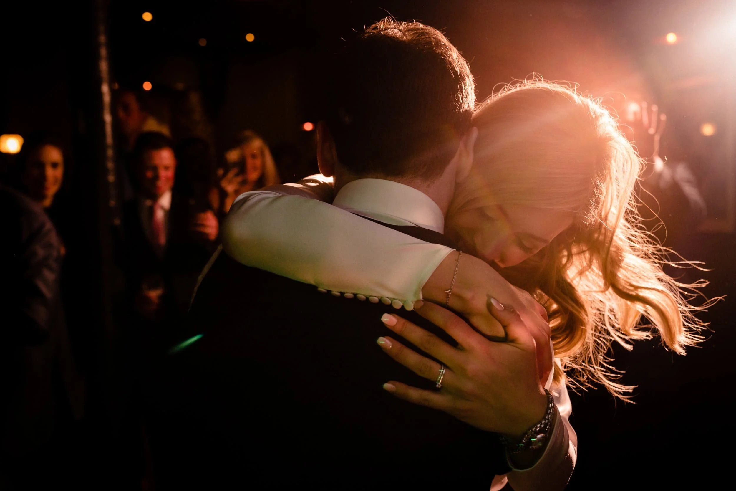 Couple holding each other close on the dance floor, backlit in warm light