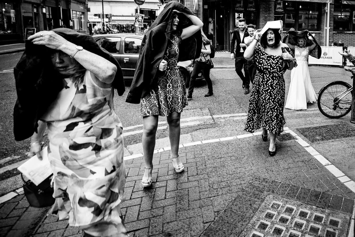 Black and white photograph of wedding guests shielding themselves from the wind on a Dublin street