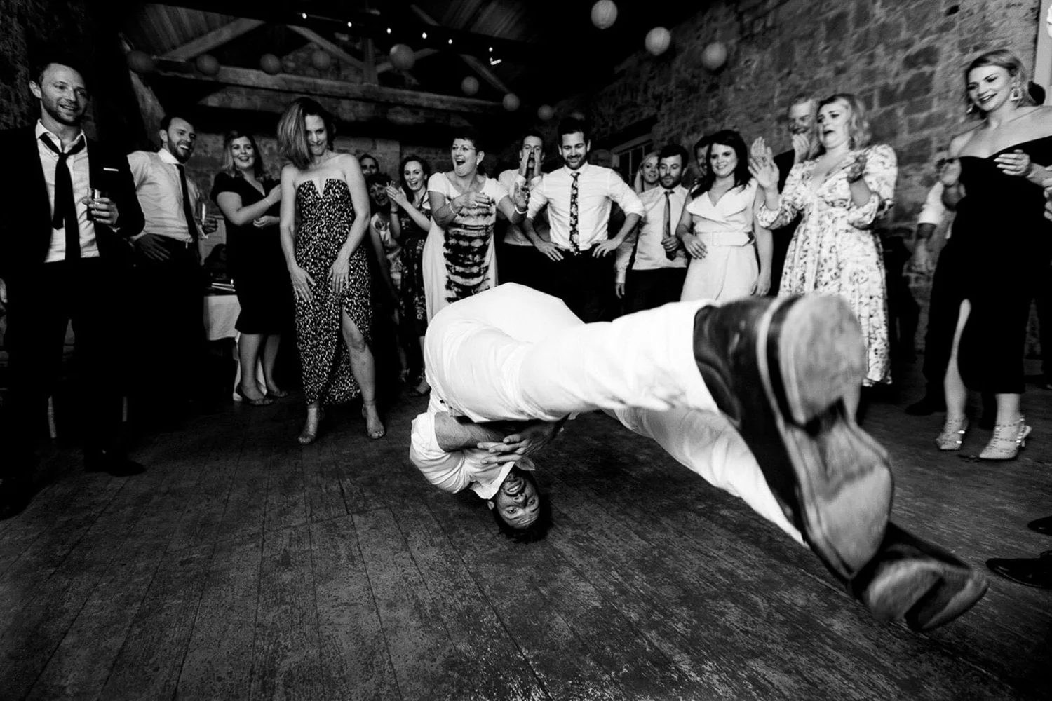 Black and white photograph of a guest breakdancing as the wedding party cheers