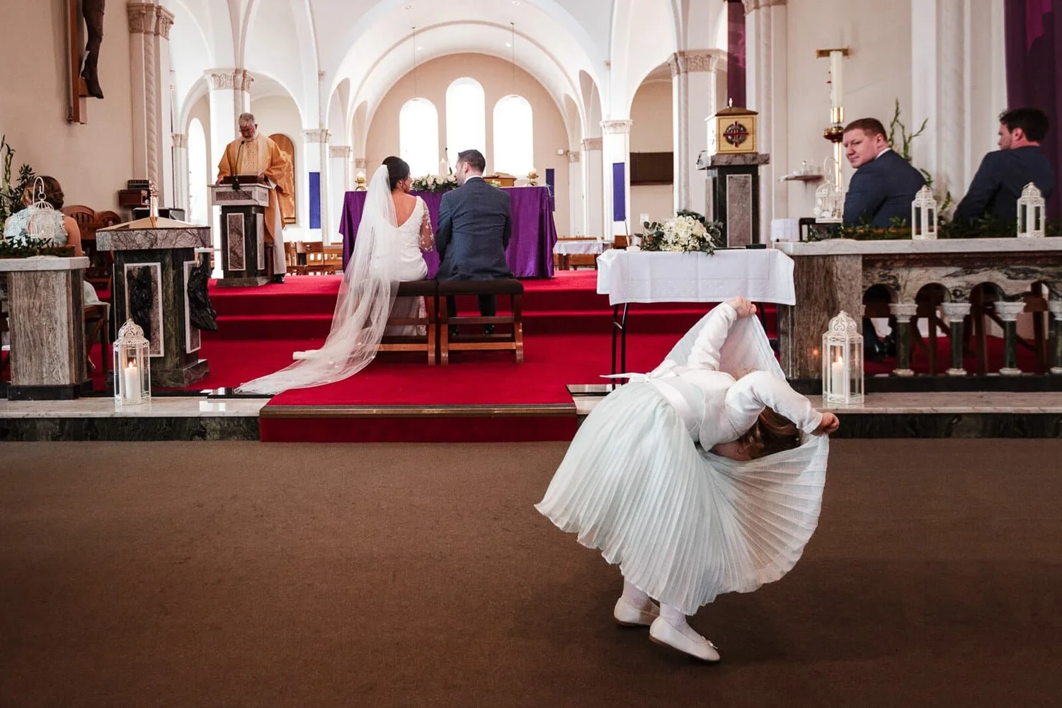 Flower girl bending to fix her dress in front of the altar during a church ceremony