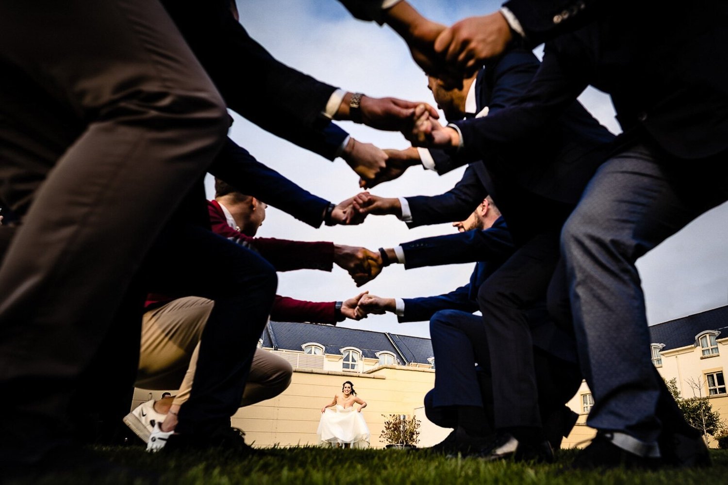 Groomsmen joining hands in a circle, photographed from below with the bride framed in the middle
