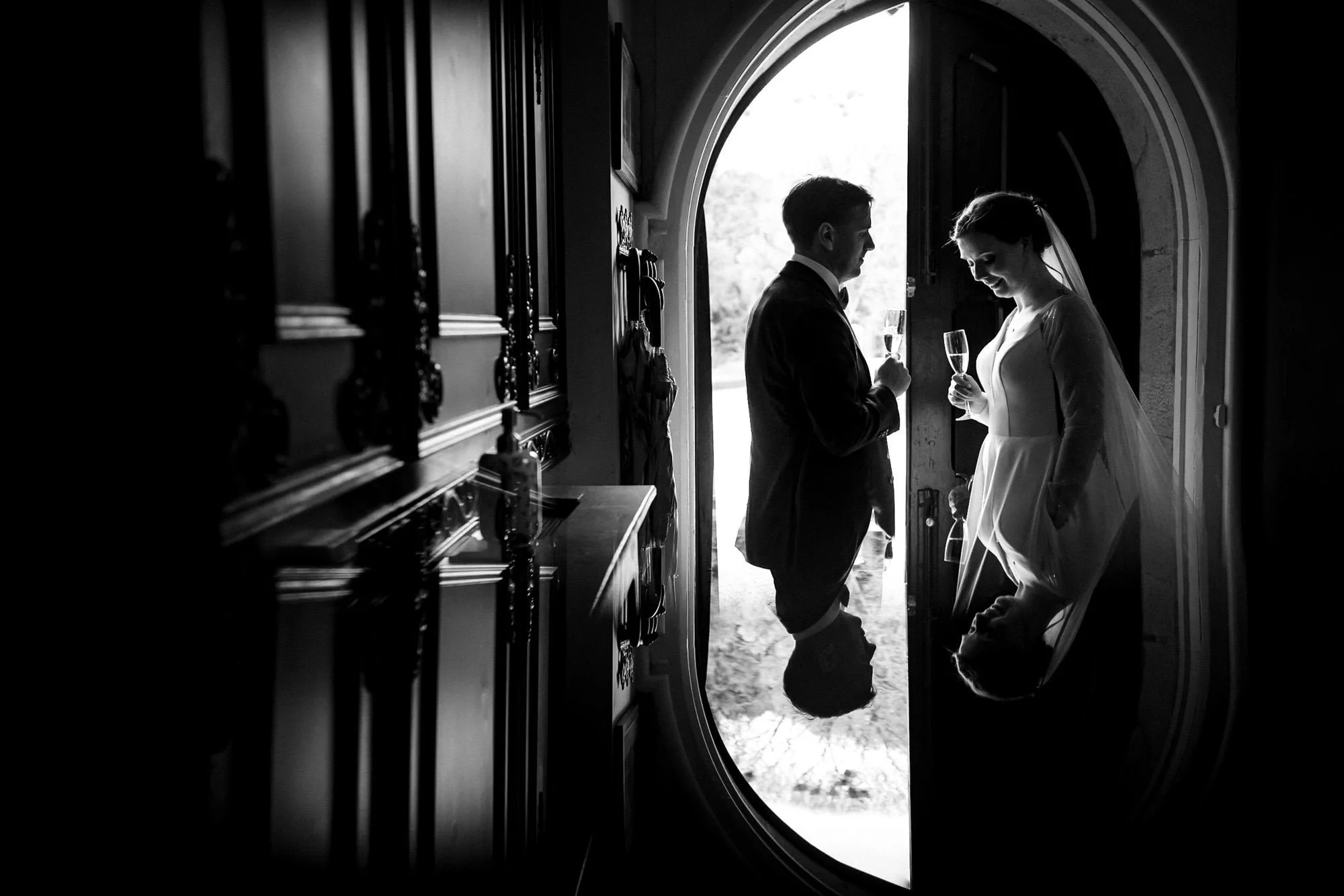 Black and white photograph of a couple in a dark doorway at Kilkea Castle, each holding a glass of champagne