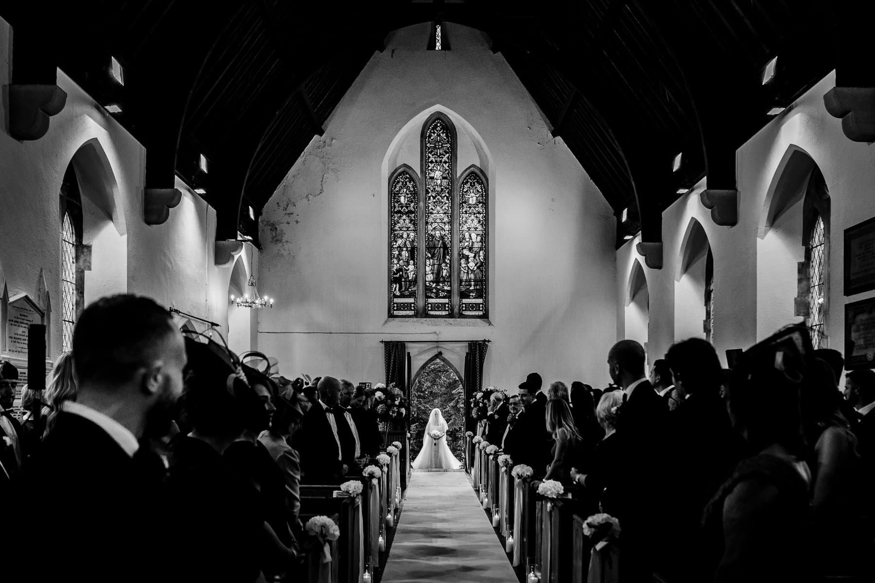 Black and white photograph of a bride walking up the aisle of a packed church