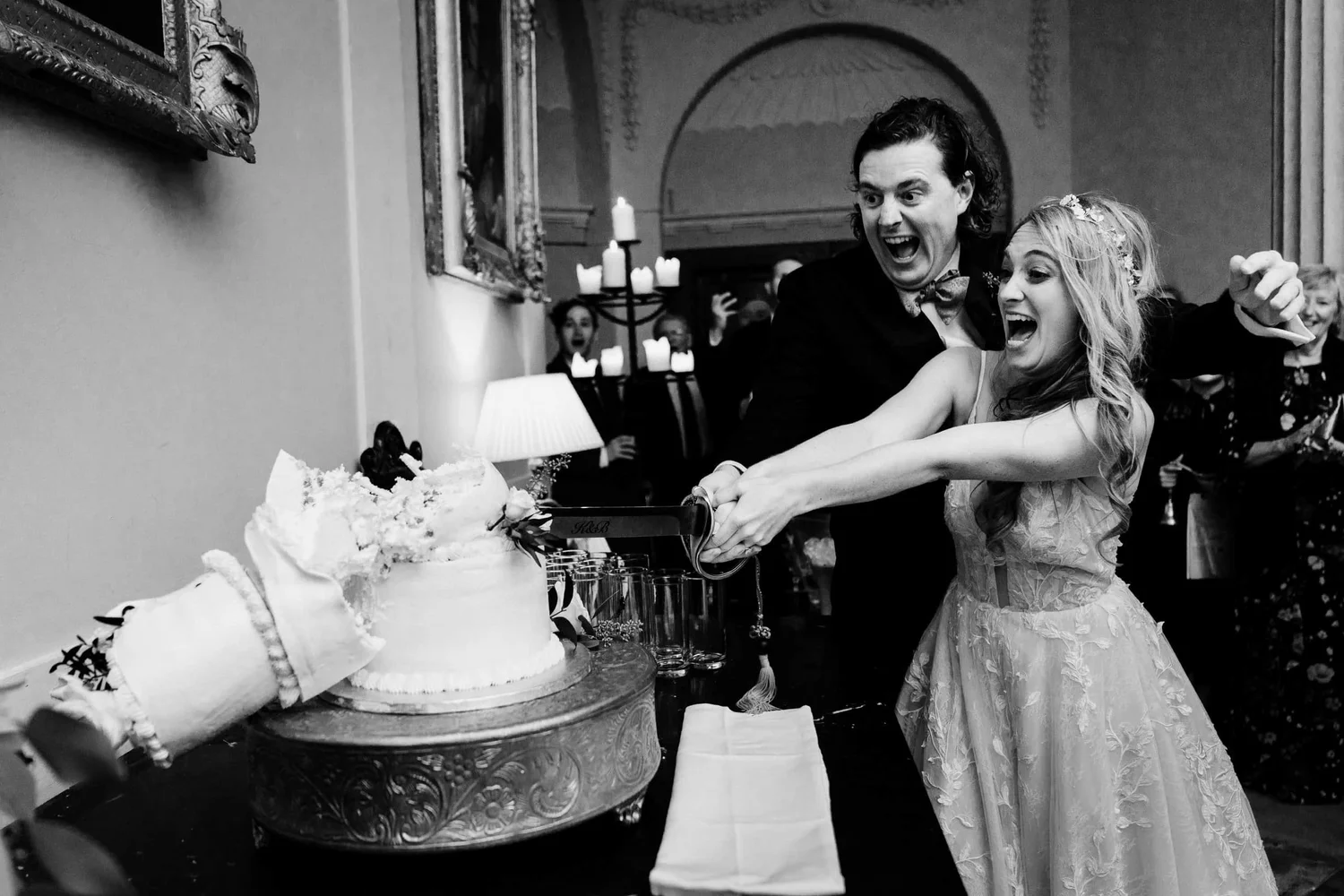 Black and white photograph of a couple reacting as their wedding cake starts to topple at Slane Castle