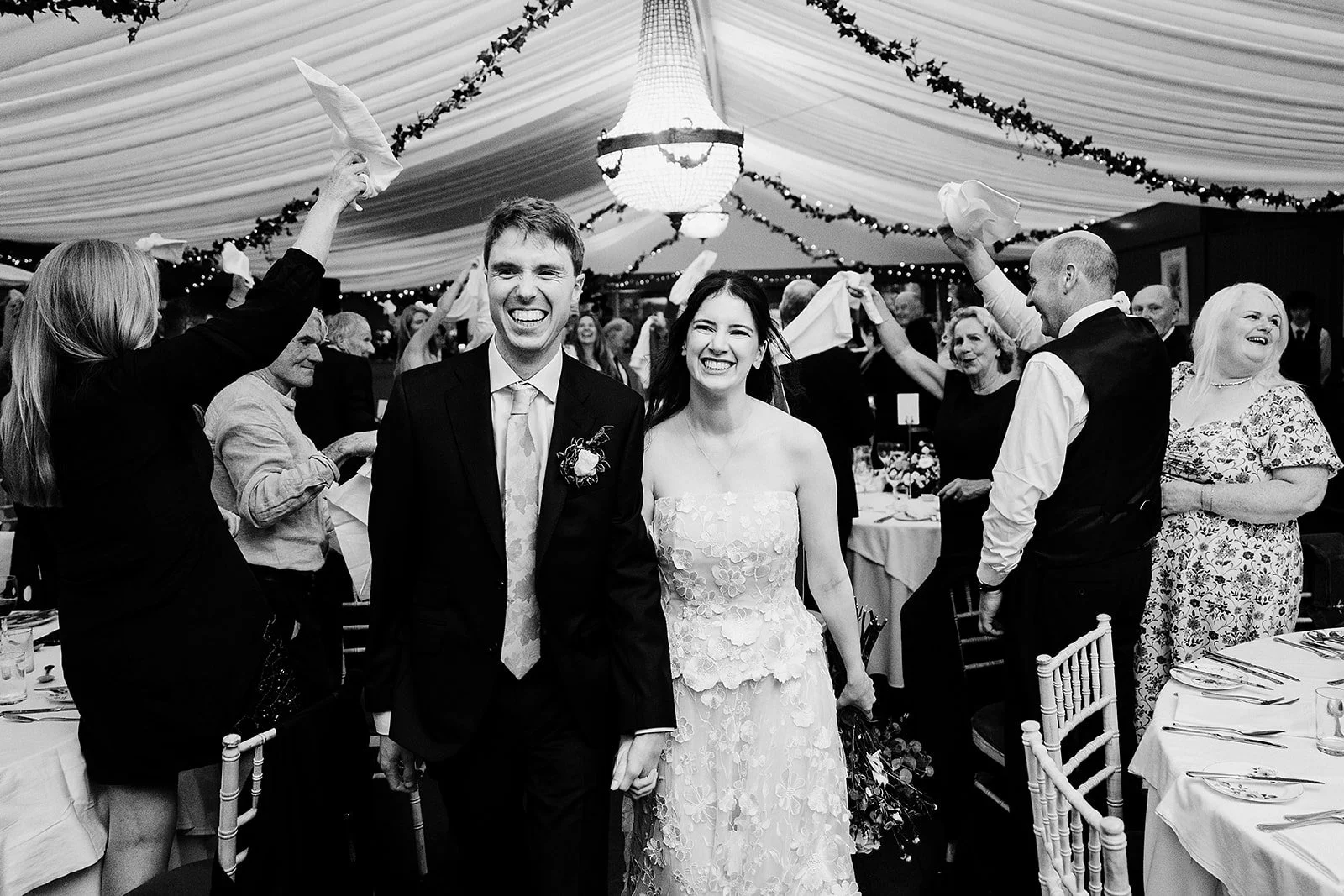 bride and groom making their entrance in the marquee in tinakilly house in wicklow while the crowd cheer with napkins in the air