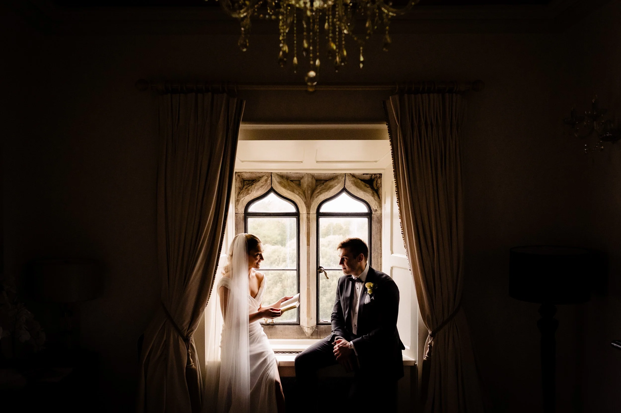 Couple sitting together in a tall arched window at Kilkea Castle, lit by soft window light