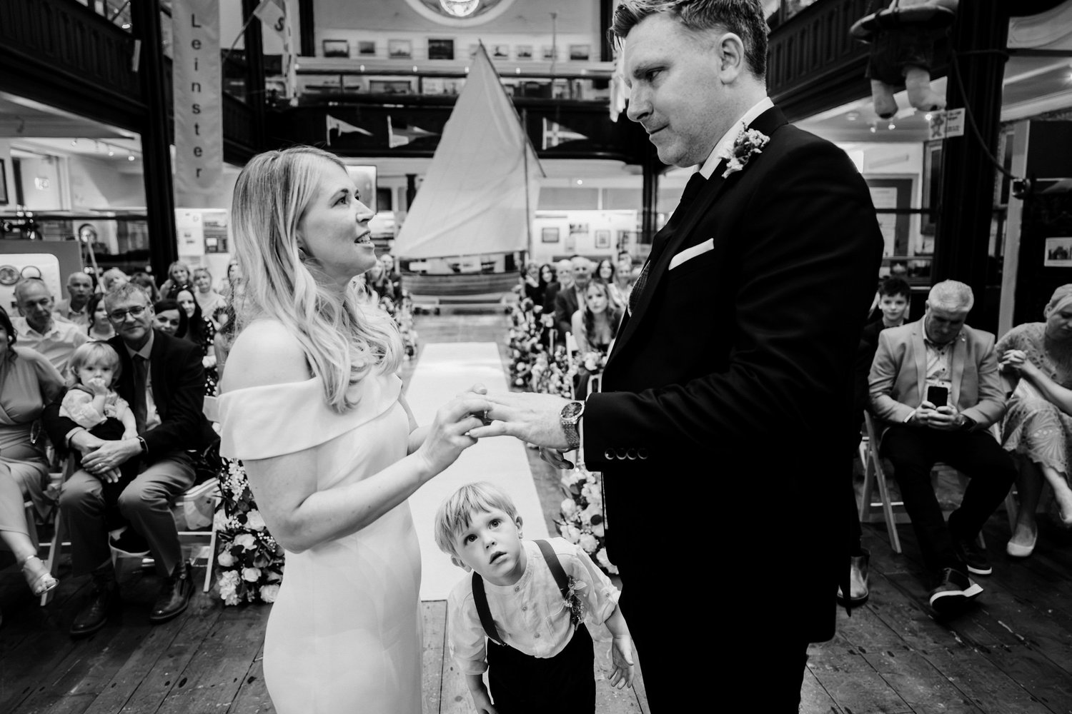 Black and white photograph of a ring exchange at the Maritime Museum as a young guest watches from below